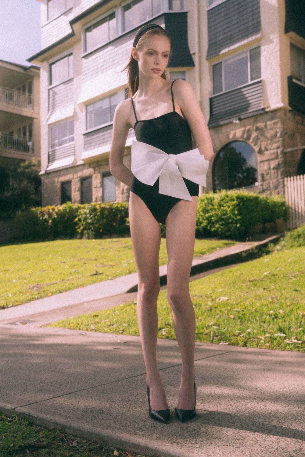 A sequence of minimalist photos showing glimpses of a figure in black swimwear posed on a suburban sidewalk.