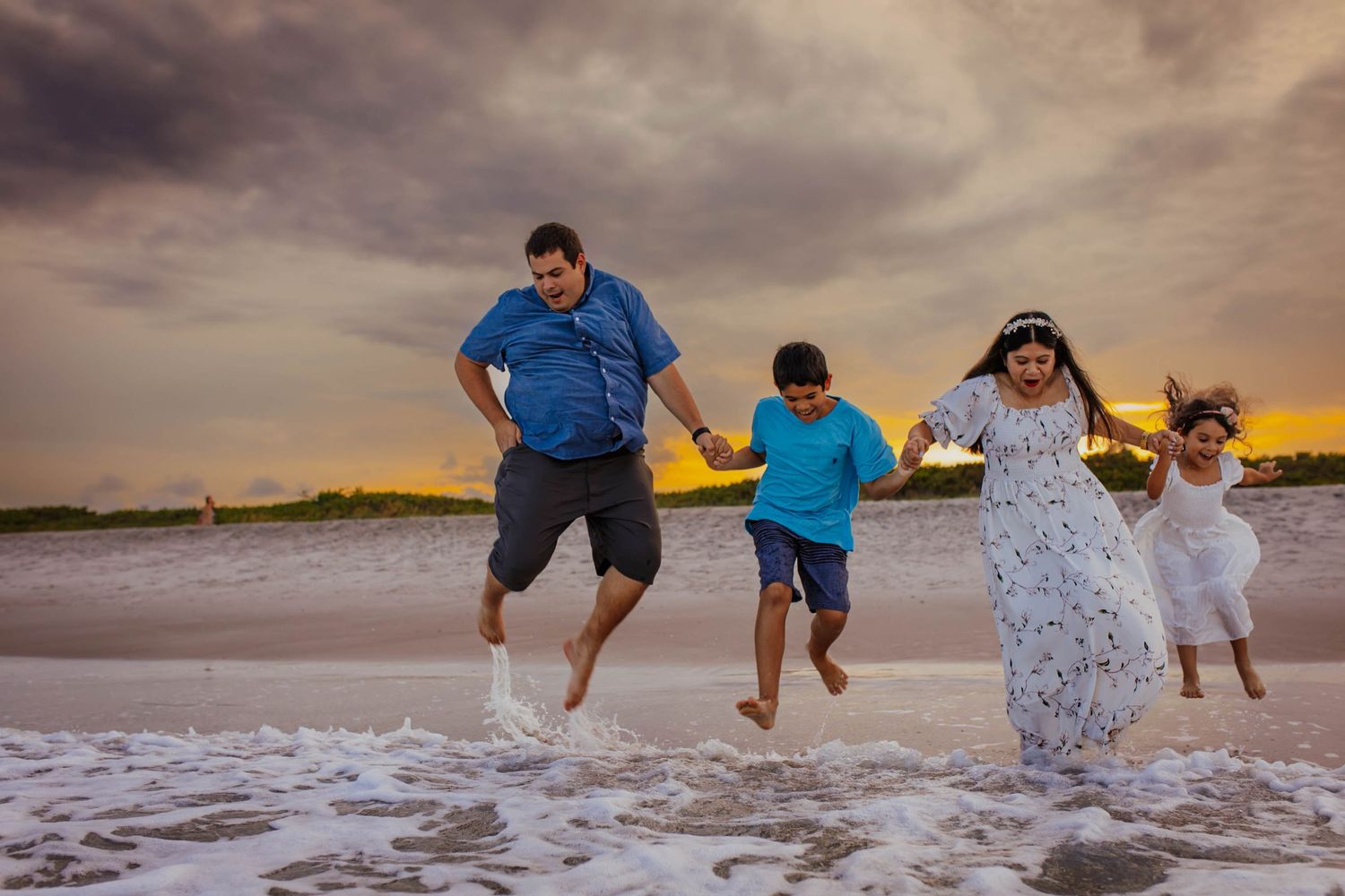 Group splashing and playing together in shallow ocean waves at sunset on a beach.