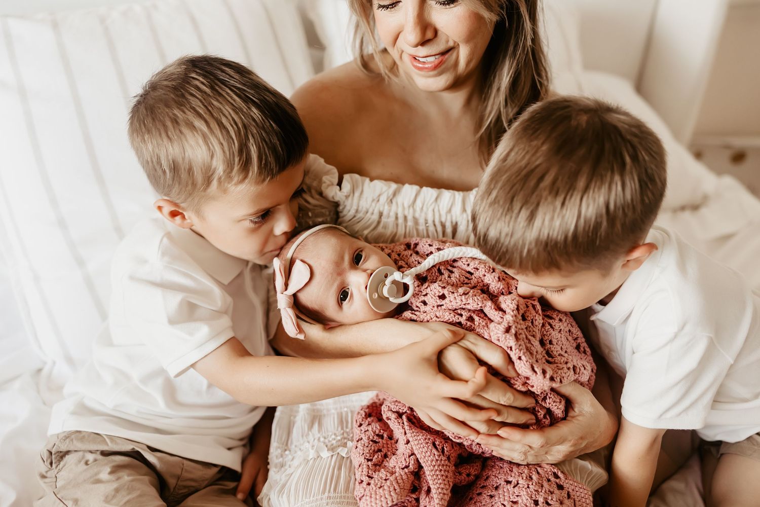Two siblings give their baby sister kisses during an Oahu newborn session.