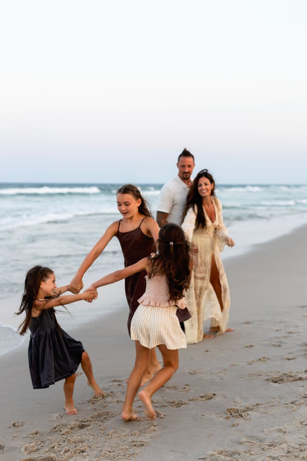 Friends dance and play together on a sandy beach with ocean waves in the background.