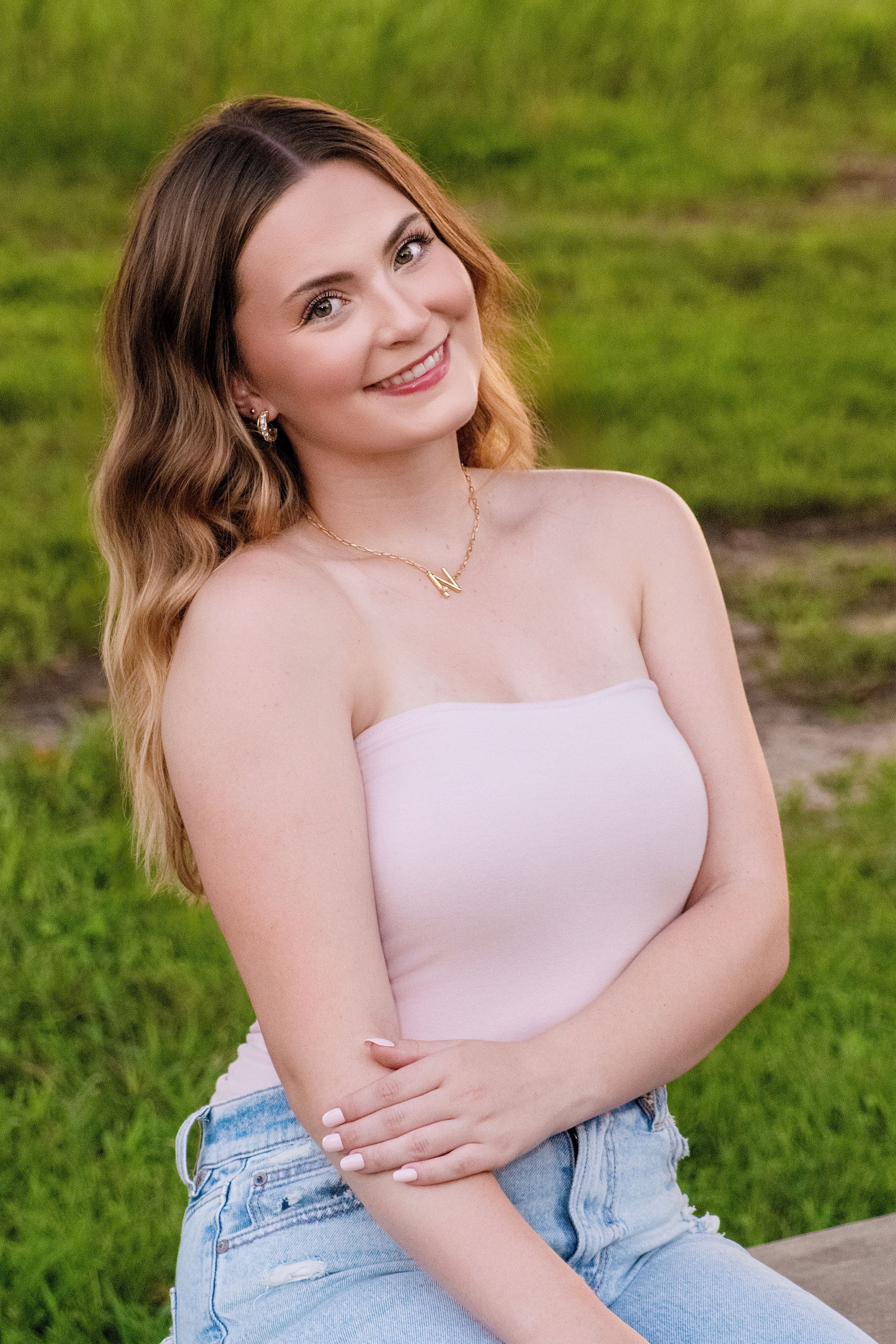 A person in a pink strapless top and denim sits casually on outdoor stone steps surrounded by green grass.