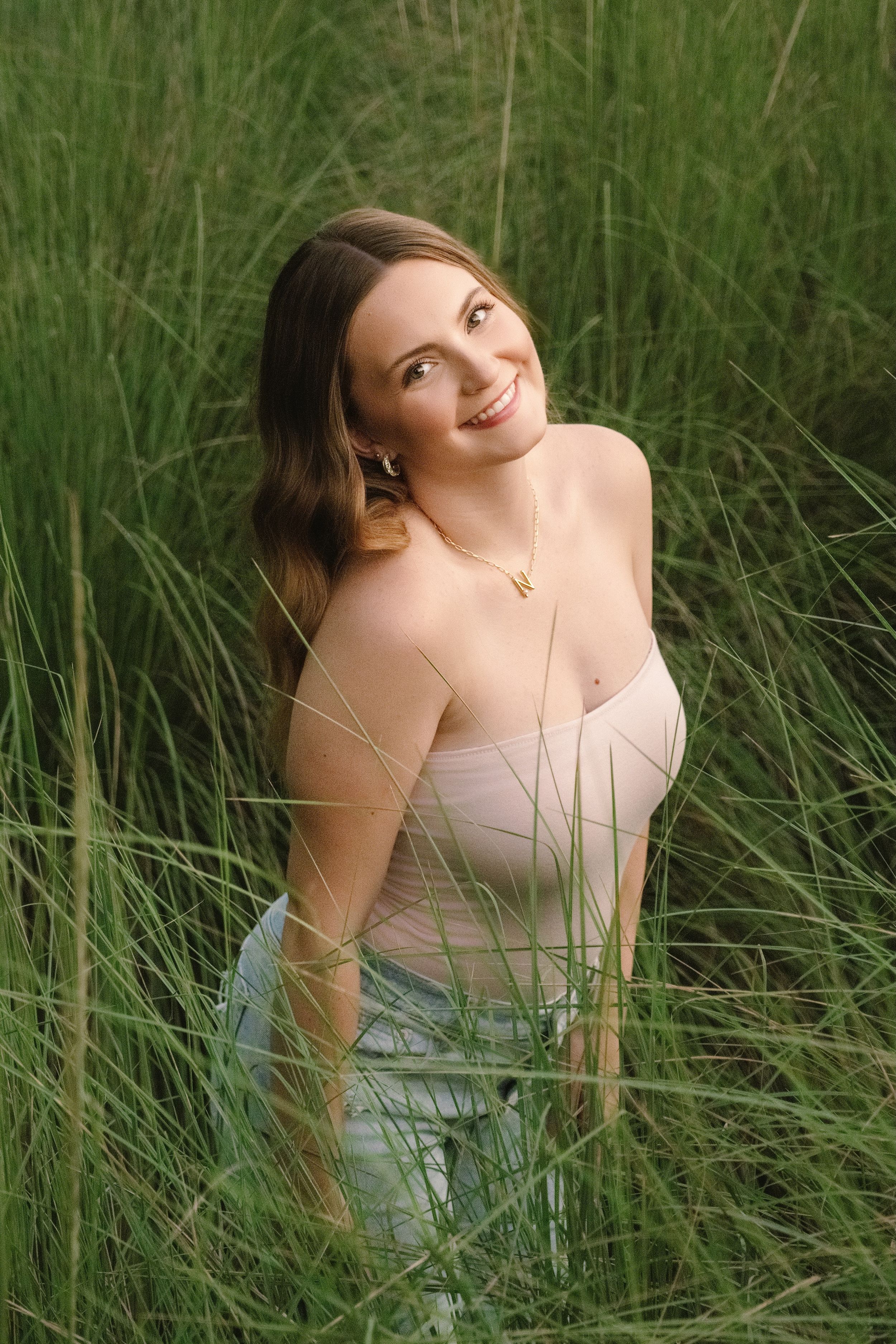 A person sits in tall grass looking up at the sky, wearing a strapless dress on a sunny day.