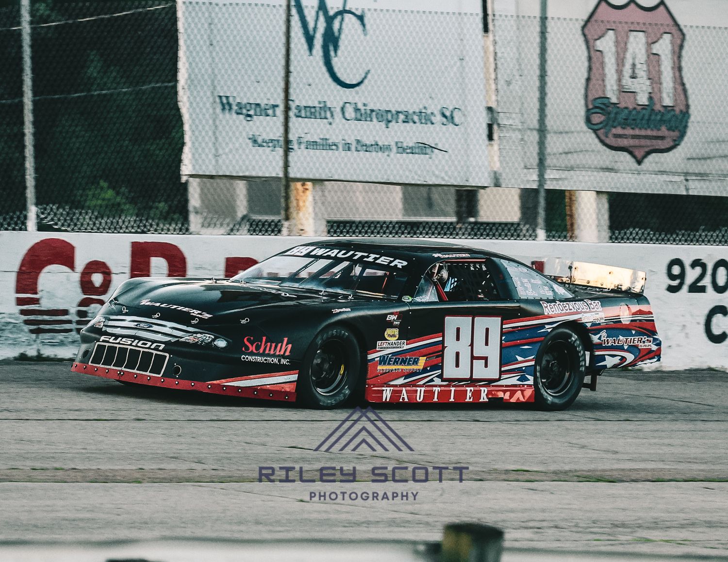 Race cars line up on the track during a stock car racing event at sunset.