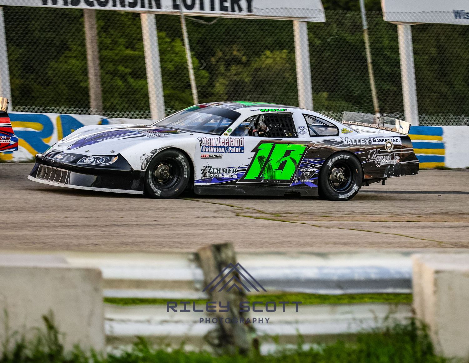 Race cars compete on an asphalt track during a motorsport event with green foliage in the background.