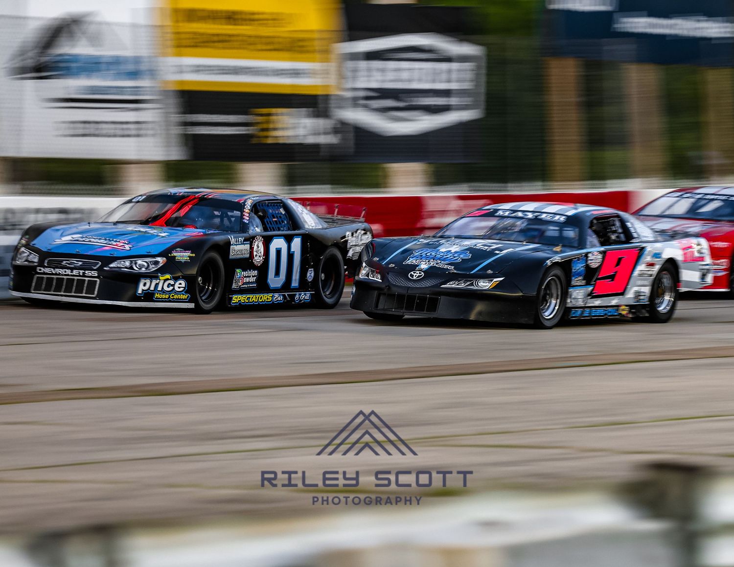 Race cars speed around a track with motion blur creating a dynamic racing scene in daytime.