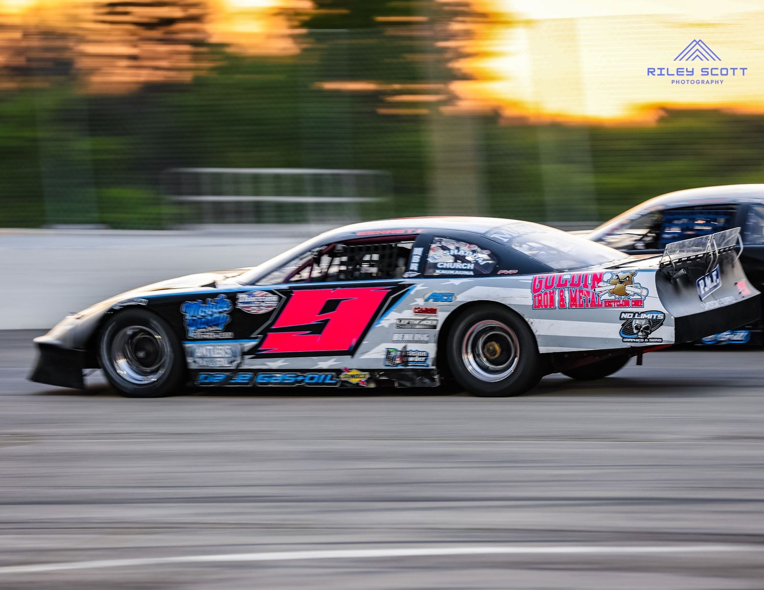 Race cars speed down a racetrack during sunset with motion blur effects creating a dramatic racing scene.