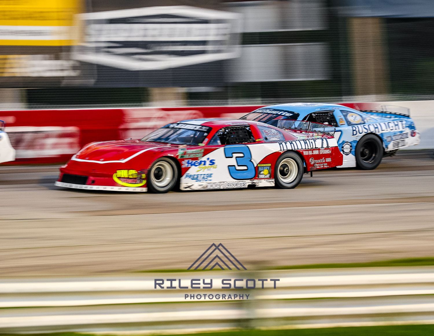 Motion-blurred racing cars speed around a racetrack with red and white barriers creating a sense of high velocity action.