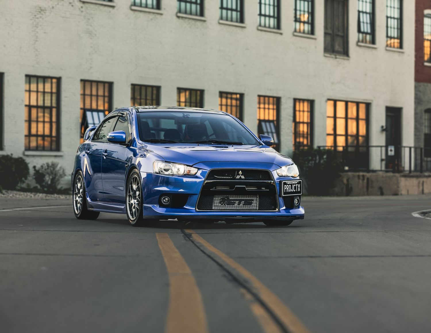 Blue Mitsubishi Lancer Evolution parked on a street in front of a brick building at dusk.