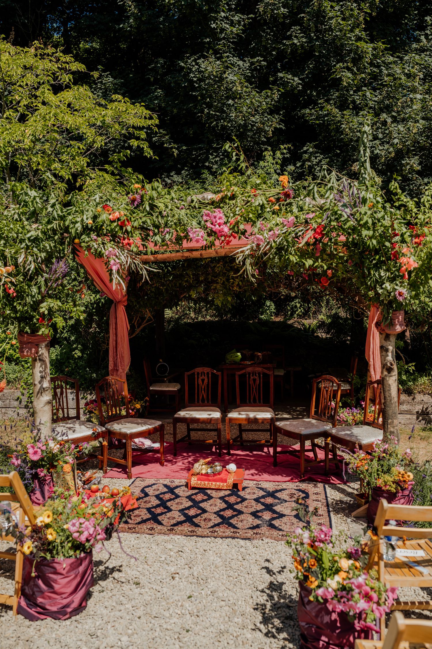 Romantic outdoor wedding venue with red drapes and floral decorations in a garden setting.