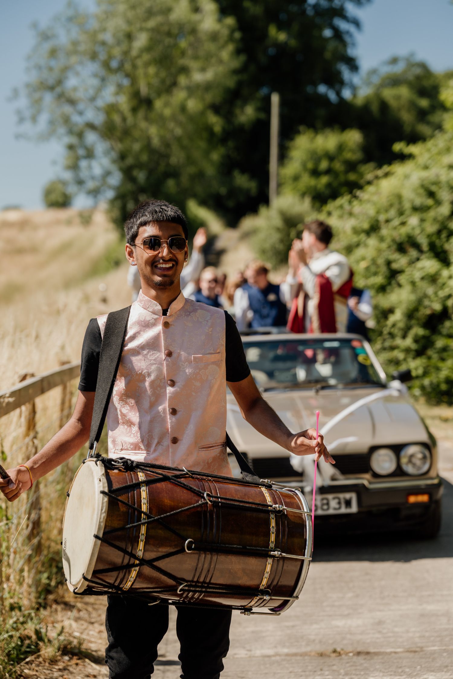A drummer performs with a traditional dhol drum outdoors during a cultural celebration.