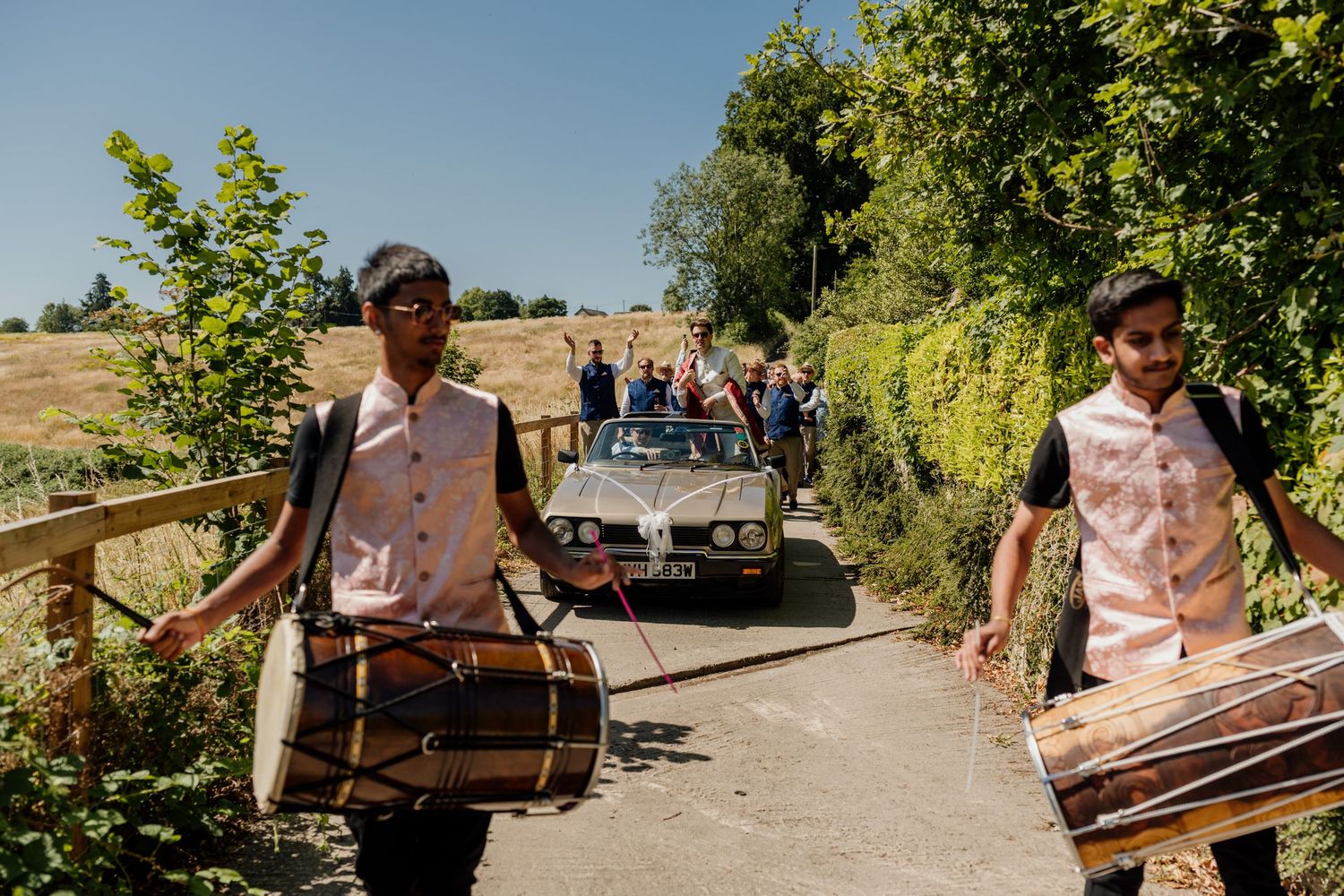 Musicians performing at an outdoor event carrying traditional instruments through a garden pathway.