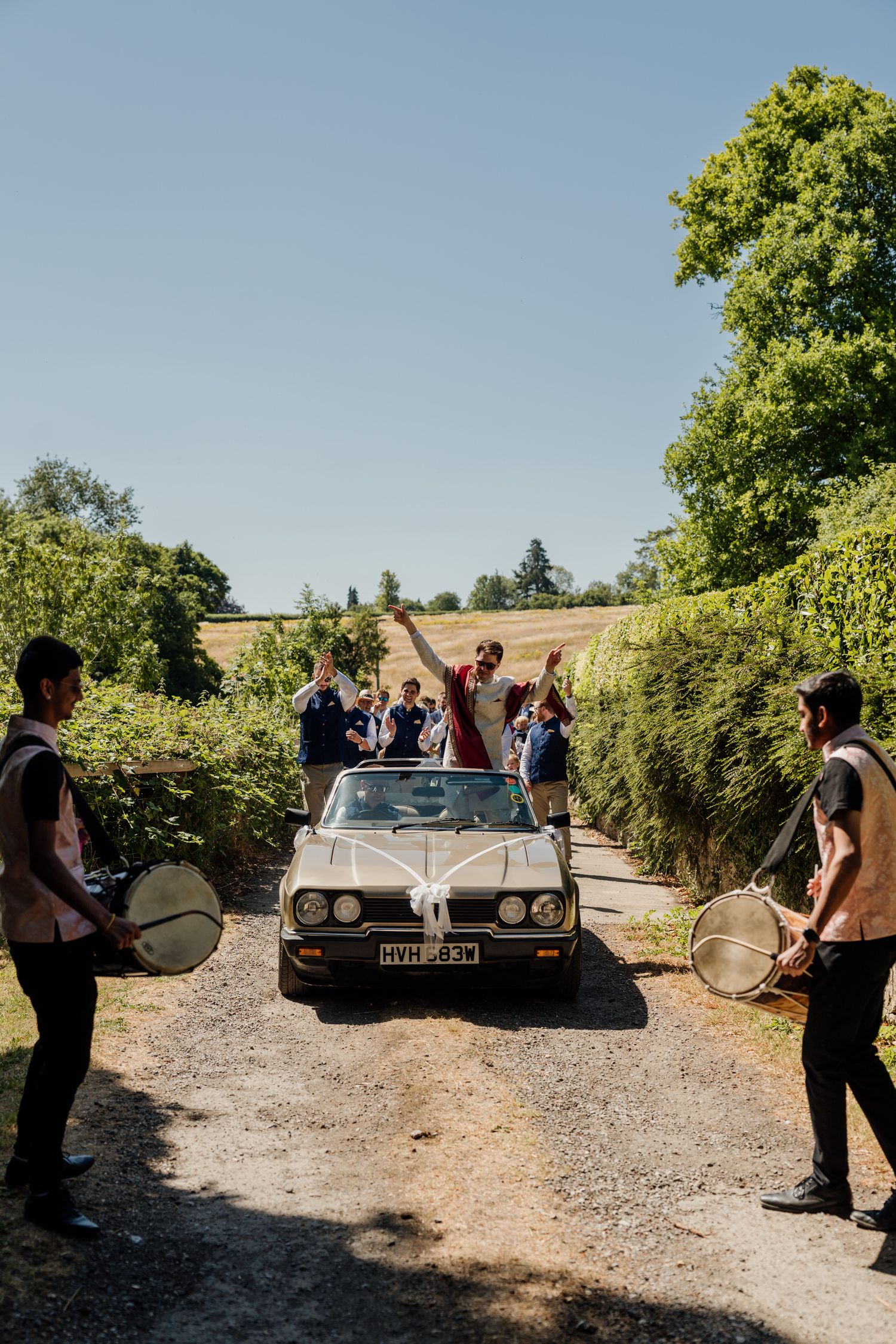 Classic vintage cars parked on a gravel driveway during a wedding celebration.