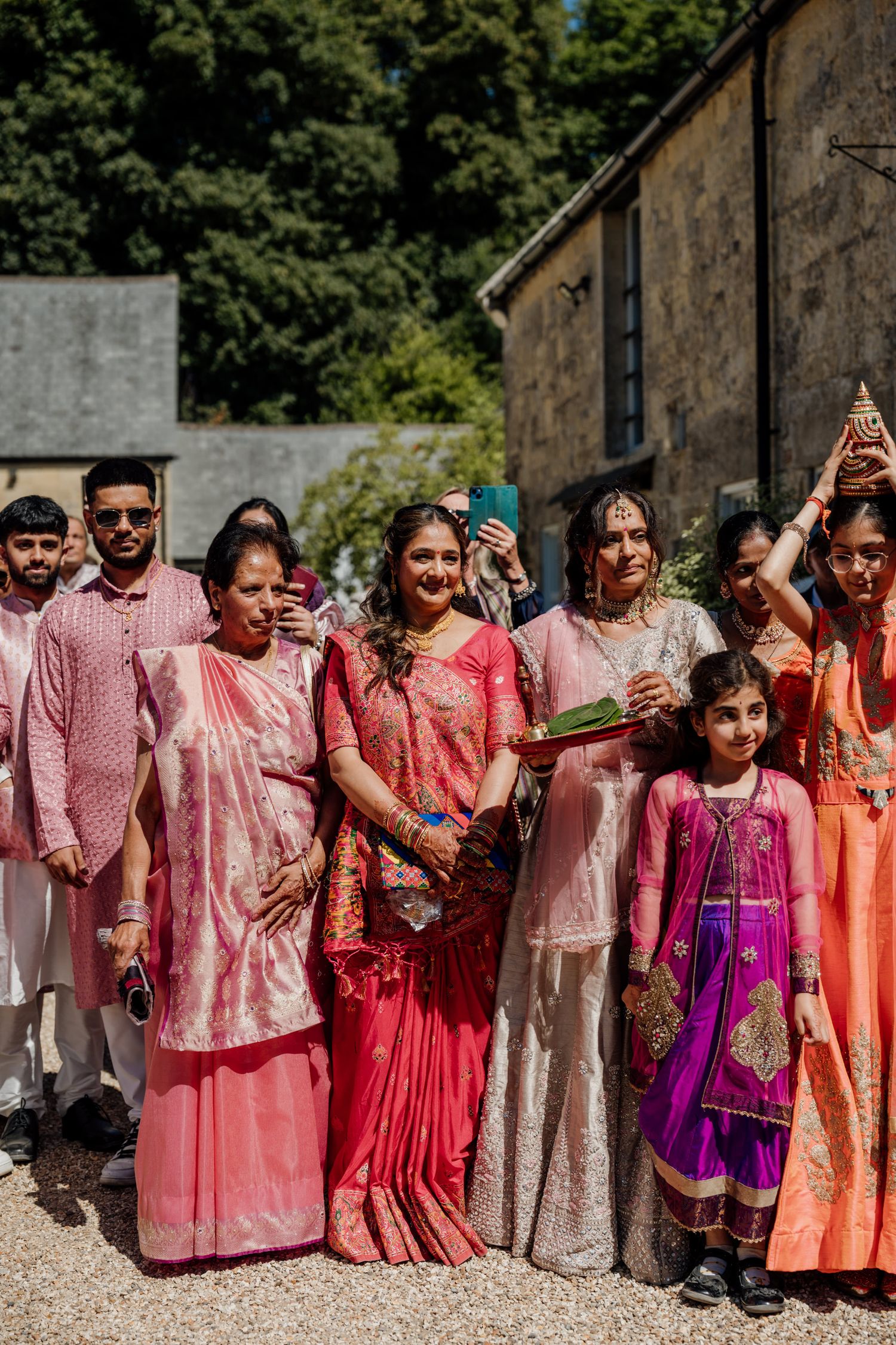 A group wearing vibrant pink and orange traditional Indian attire poses together at an outdoor event.