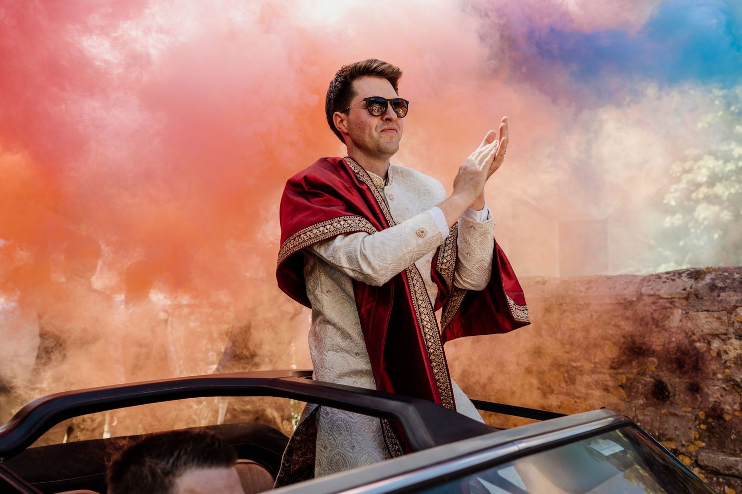 Festive scene with pink and blue smoke effects surrounding a classic car at sunset.
