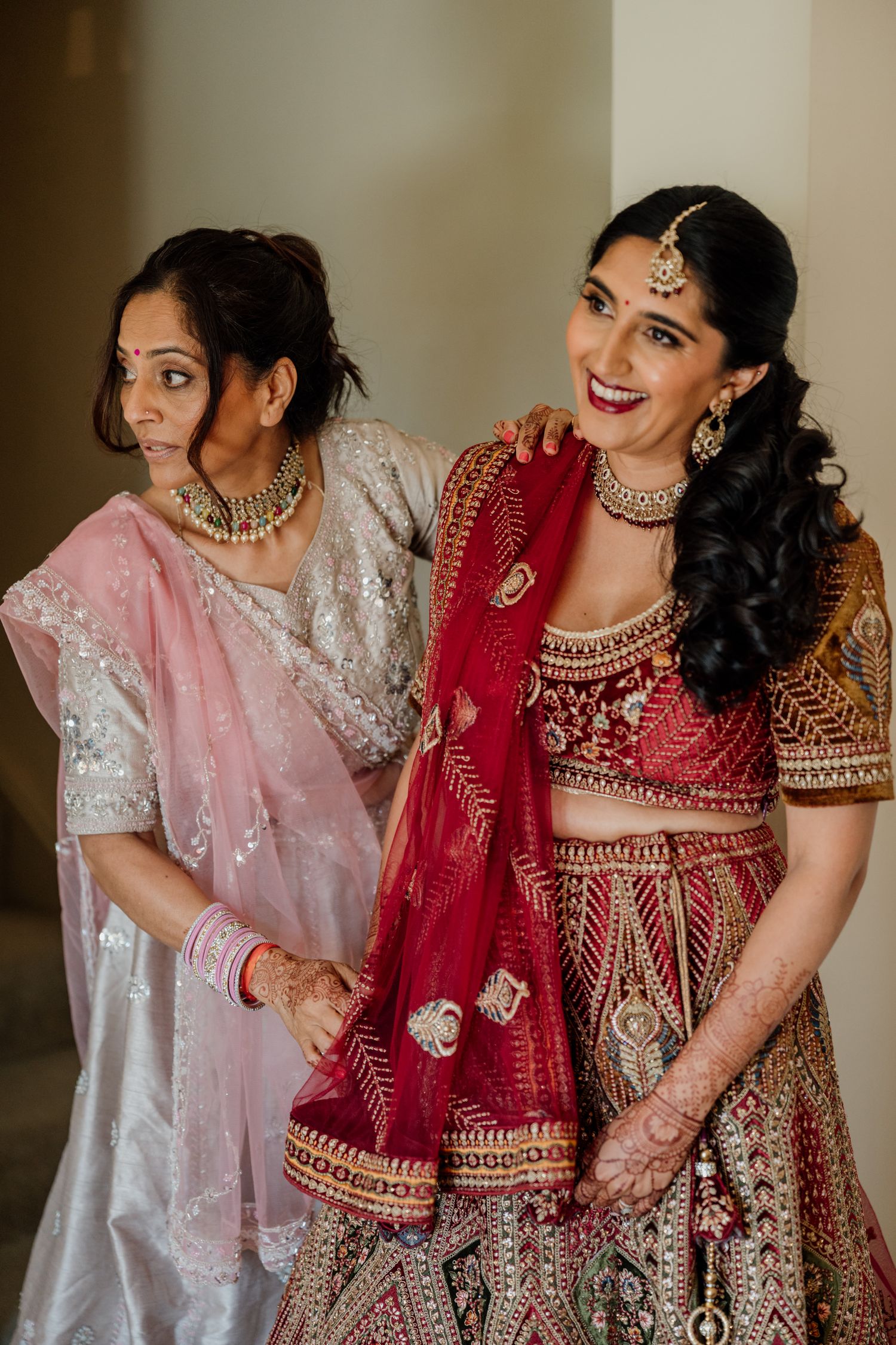 A traditional Indian bridal scene with ornate red lehenga, pink dupatta and detailed jewelry and embroidery work.