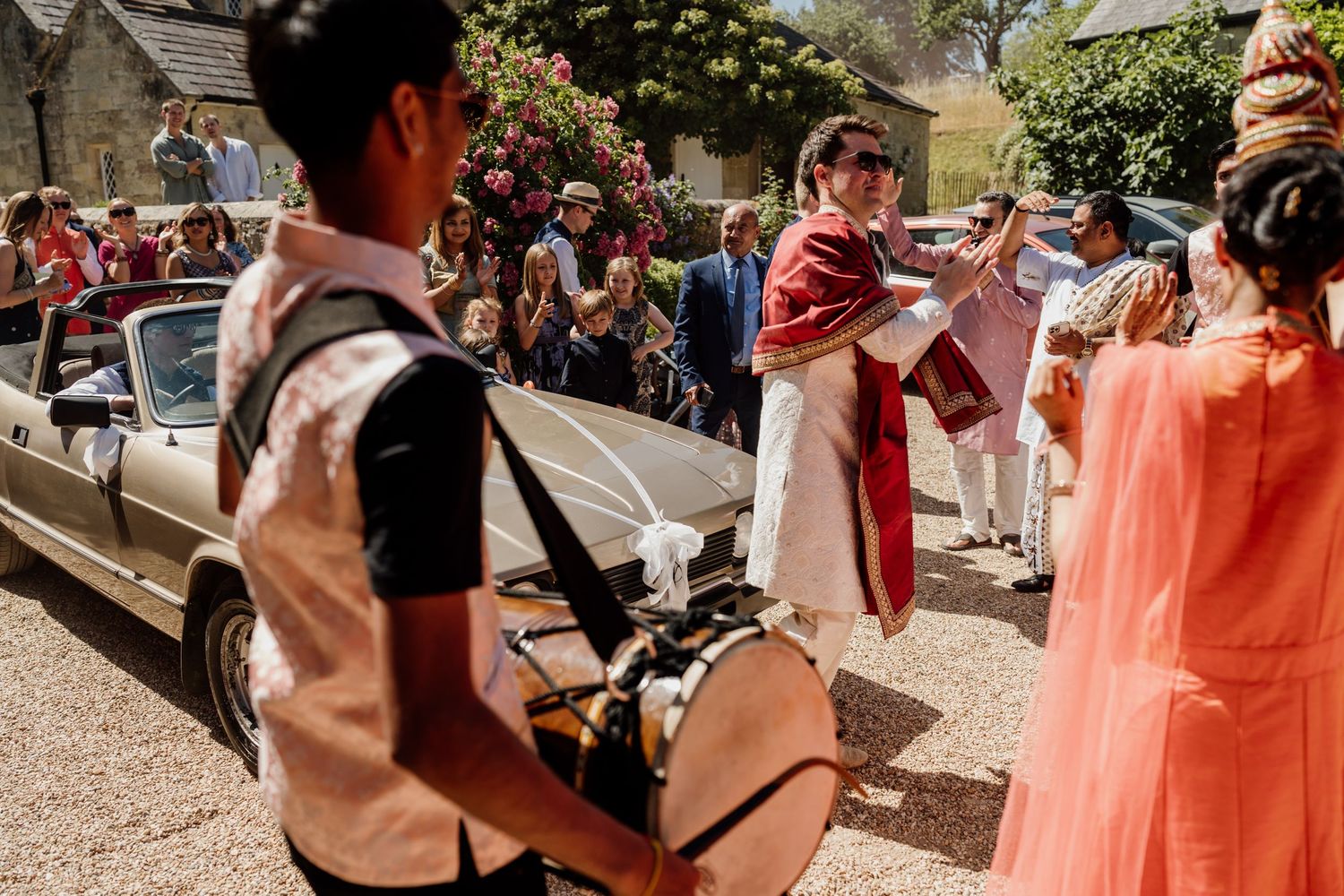Colorfully dressed wedding guests dance and celebrate outdoors at a festive summer celebration.
