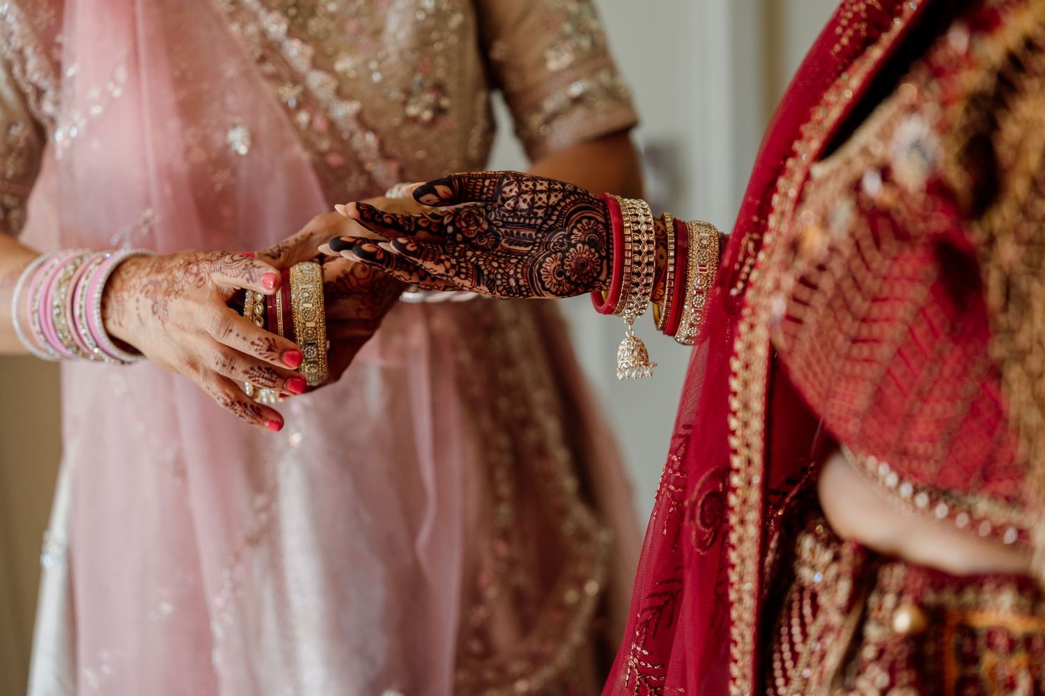 Detailed shot of hands wearing traditional Indian wedding jewelry and henna designs.