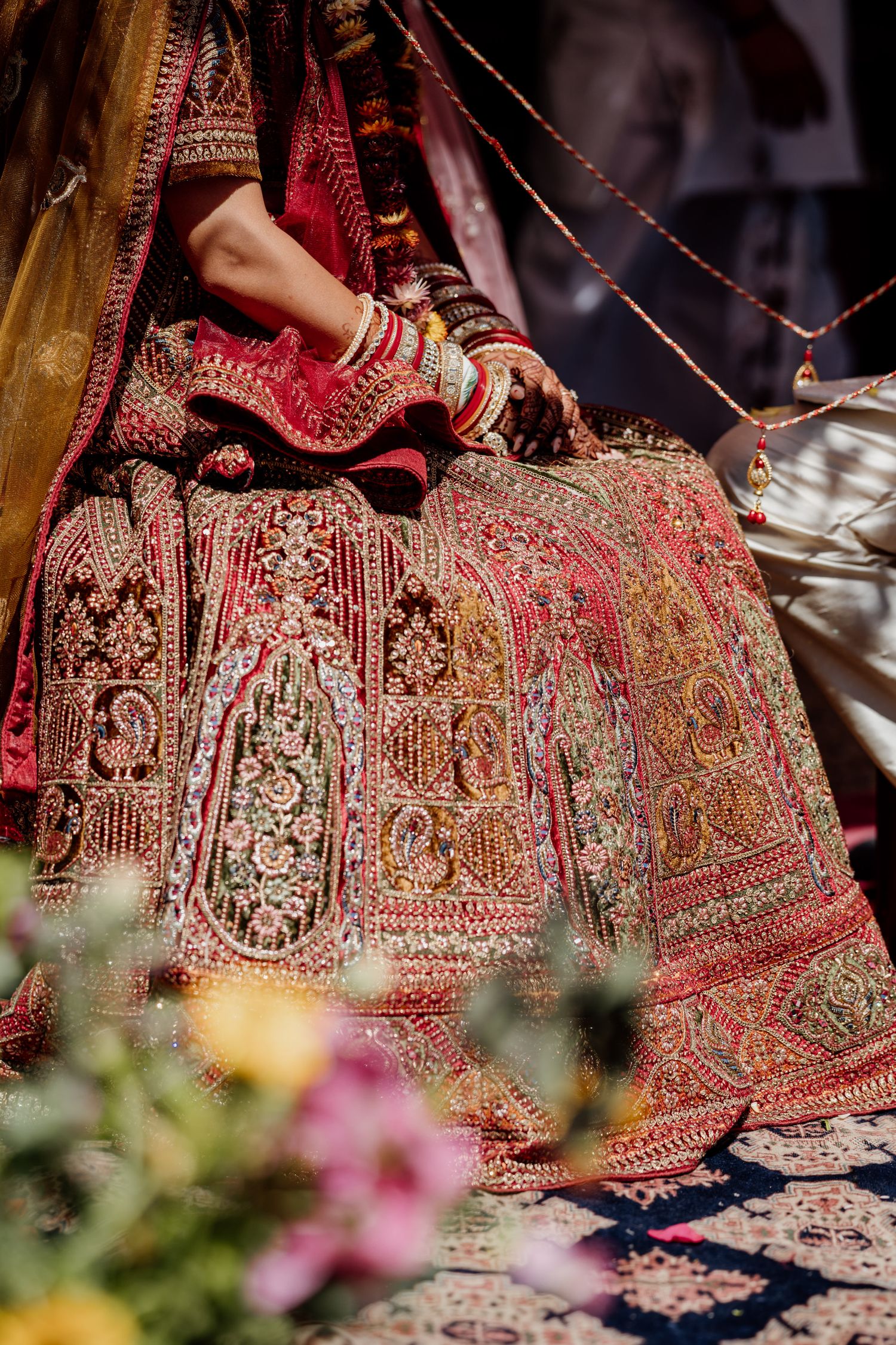 Close-up details of an ornate red and gold embroidered Indian wedding lehenga skirt spread on the ground.