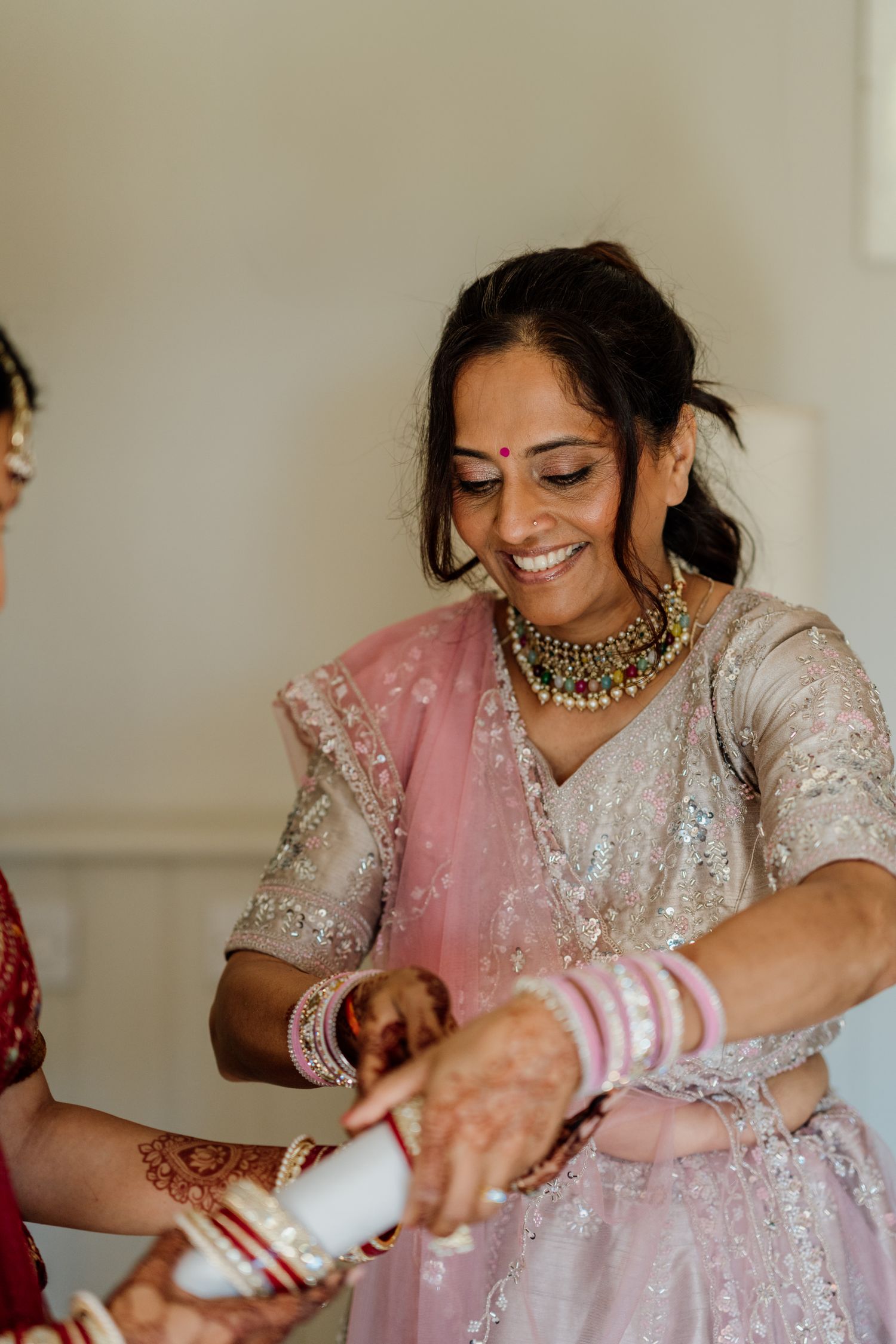 Close-up shots show hands adorned with white wedding bangles and henna designs against elegant white and pink attire.