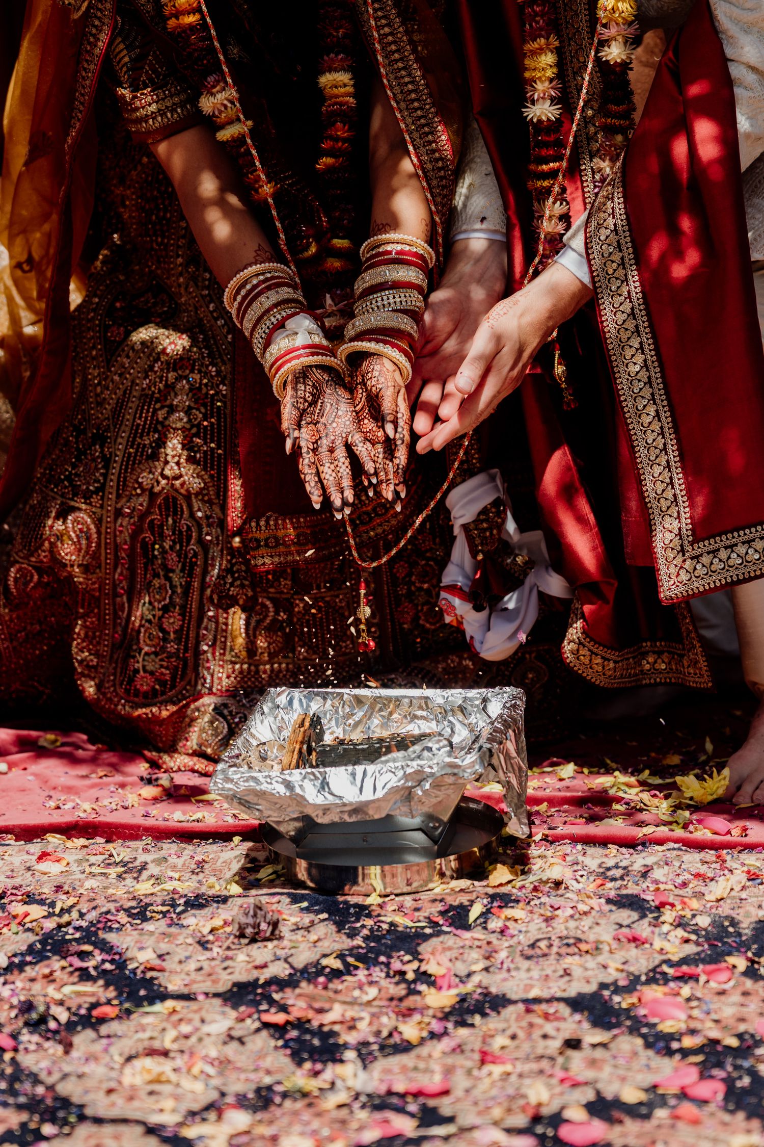 Intricate henna designs and traditional Indian wedding attire displayed during a ceremony with rose petals scattered on floor.