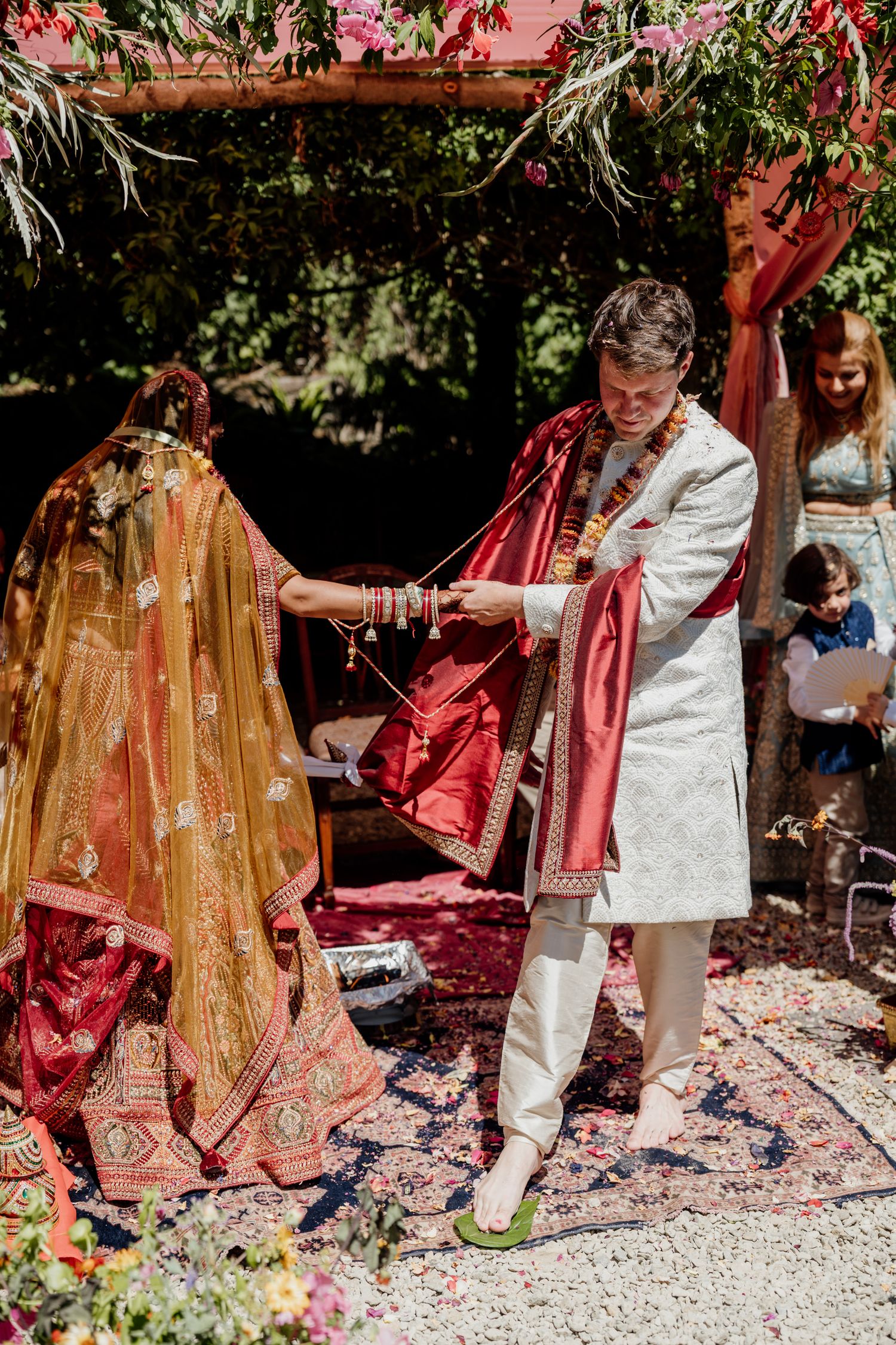 Traditional Indian wedding ceremony featuring elegant red and gold fabrics being displayed outdoors in a garden setting.