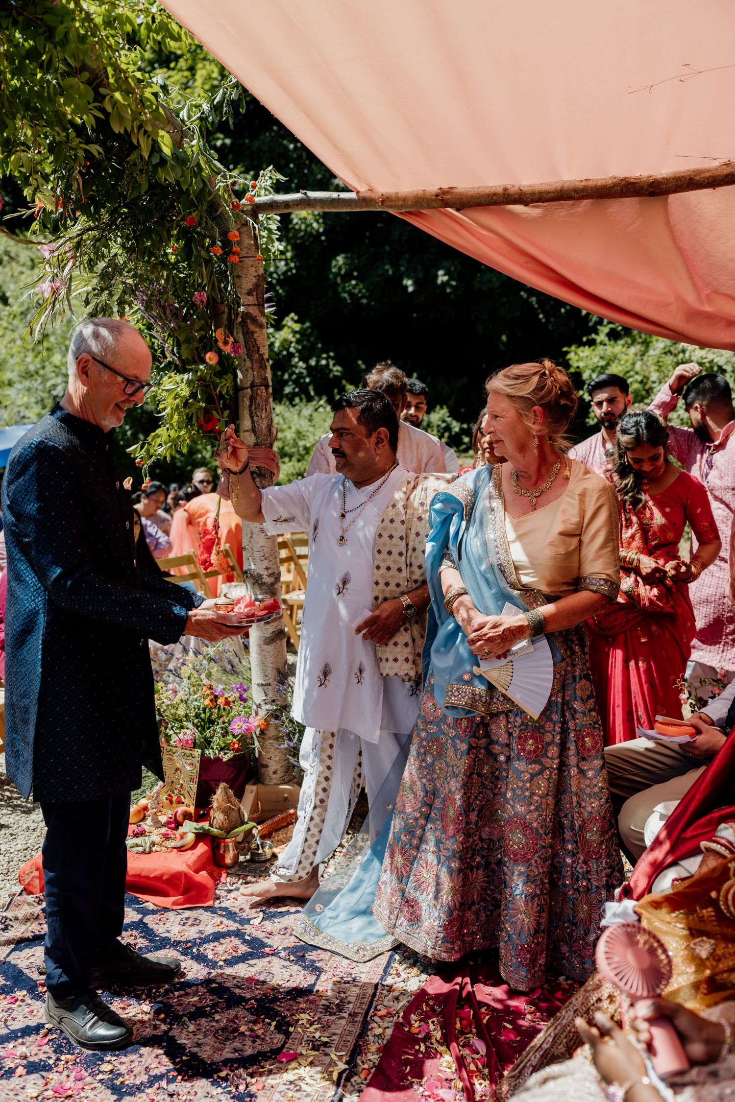 Traditional outdoor ceremony with guests gathered under a peach-colored tent canopy.