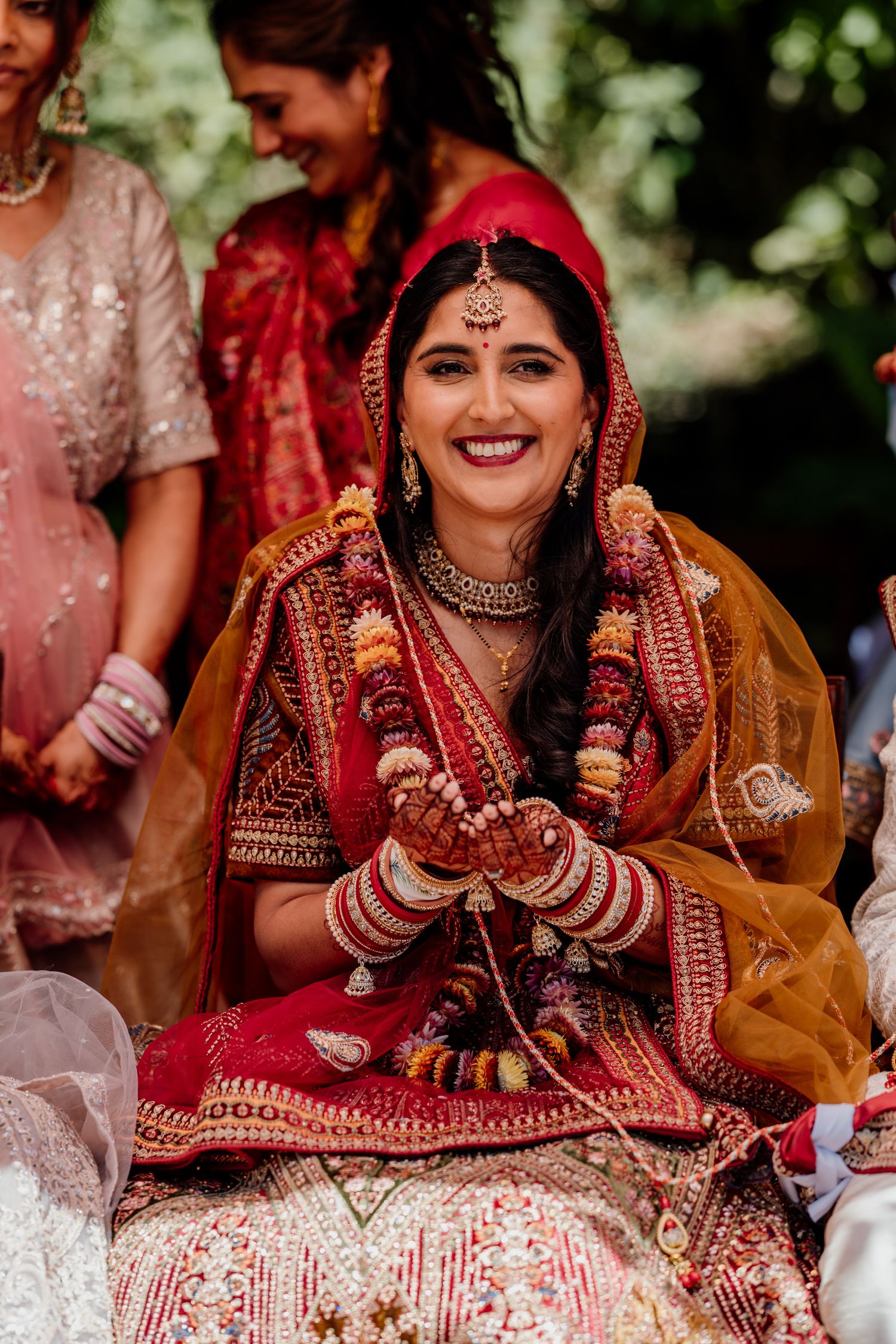 Traditional Indian bride wearing intricate red wedding attire and jewelry smiles during wedding ceremony celebrations.