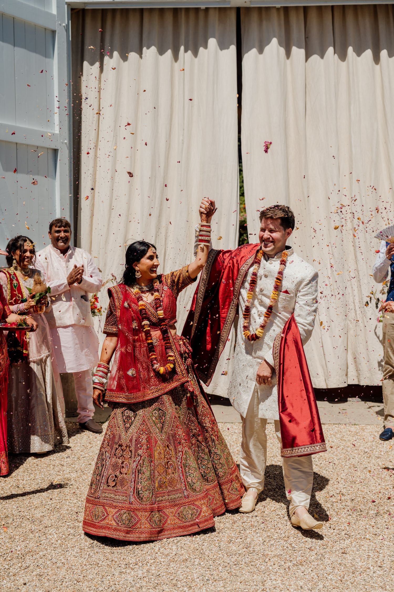 Wedding party celebrates with confetti and dance moves against white backdrop during festive ceremony.