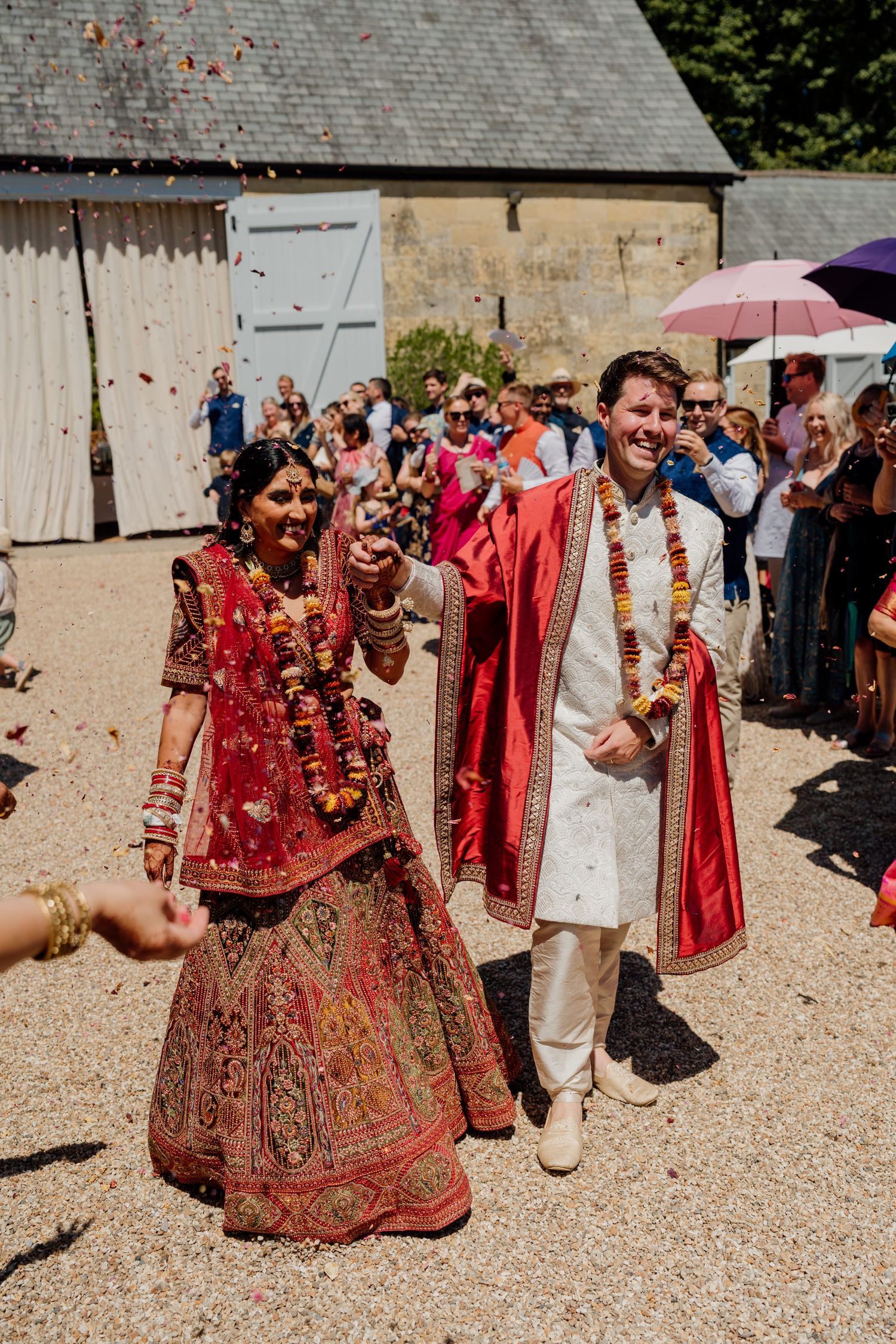 Wedding celebration with guests throwing colorful confetti around a couple in traditional Indian attire.