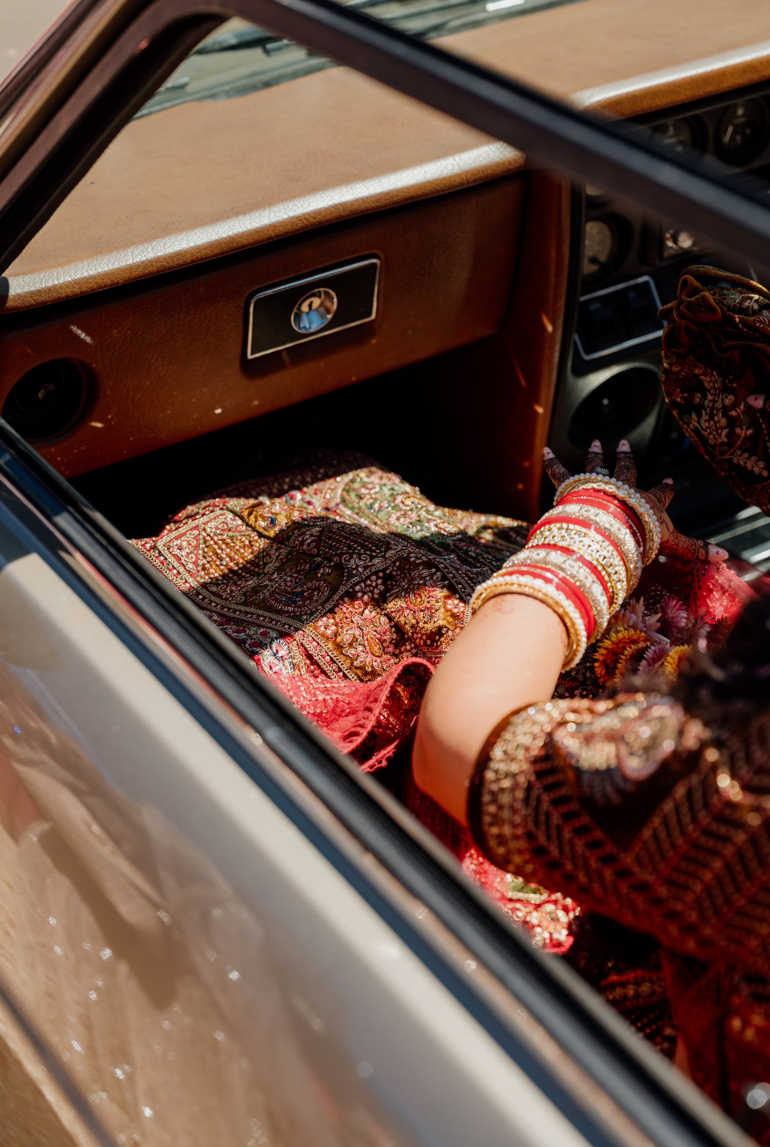 Close-up of elaborately decorated hands with henna and bangles inside a vehicle.