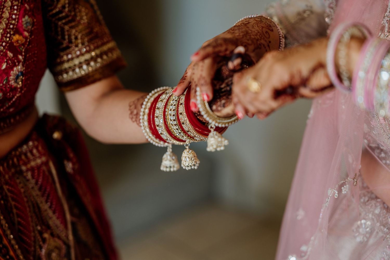 Intricate bride's mehndi henna design on hands adorned with red bangles and traditional Indian wedding jewelry.