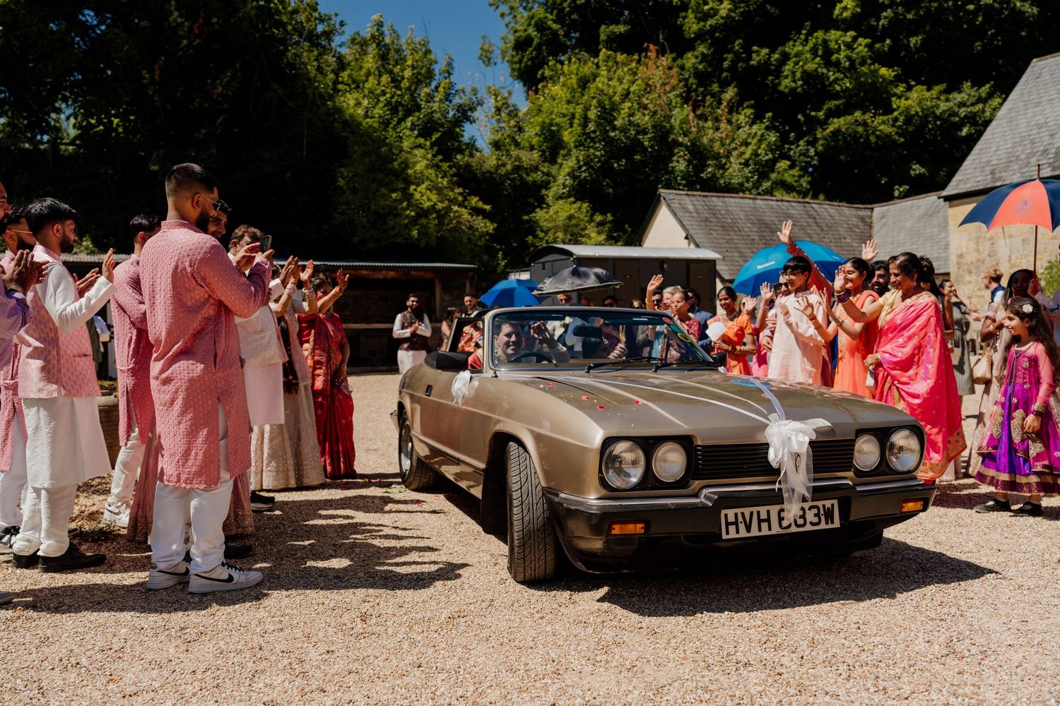 Classic vintage cars parked at a sunny outdoor wedding venue with trees in the background.