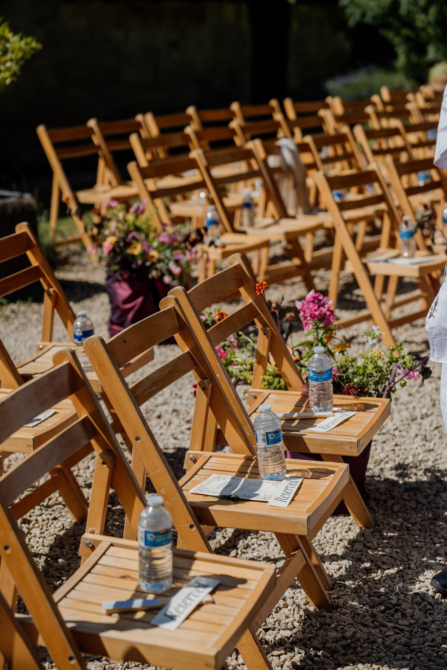 Wooden folding chairs decorated with floral arrangements set up for an outdoor wedding ceremony.