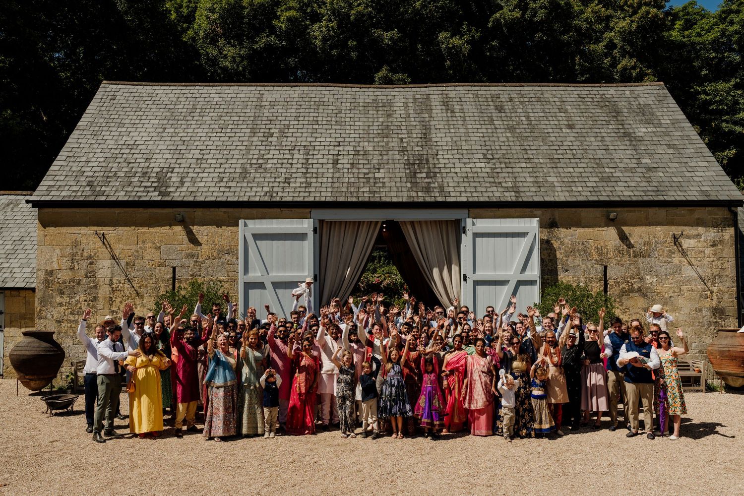 Large group photo of wedding guests gathered outside a rustic stone building during a celebration.