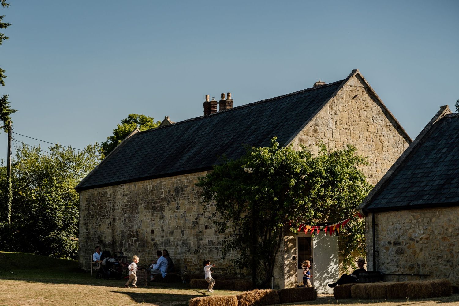A panoramic sequence showing old stone barn buildings in daytime with green foliage against a blue sky.