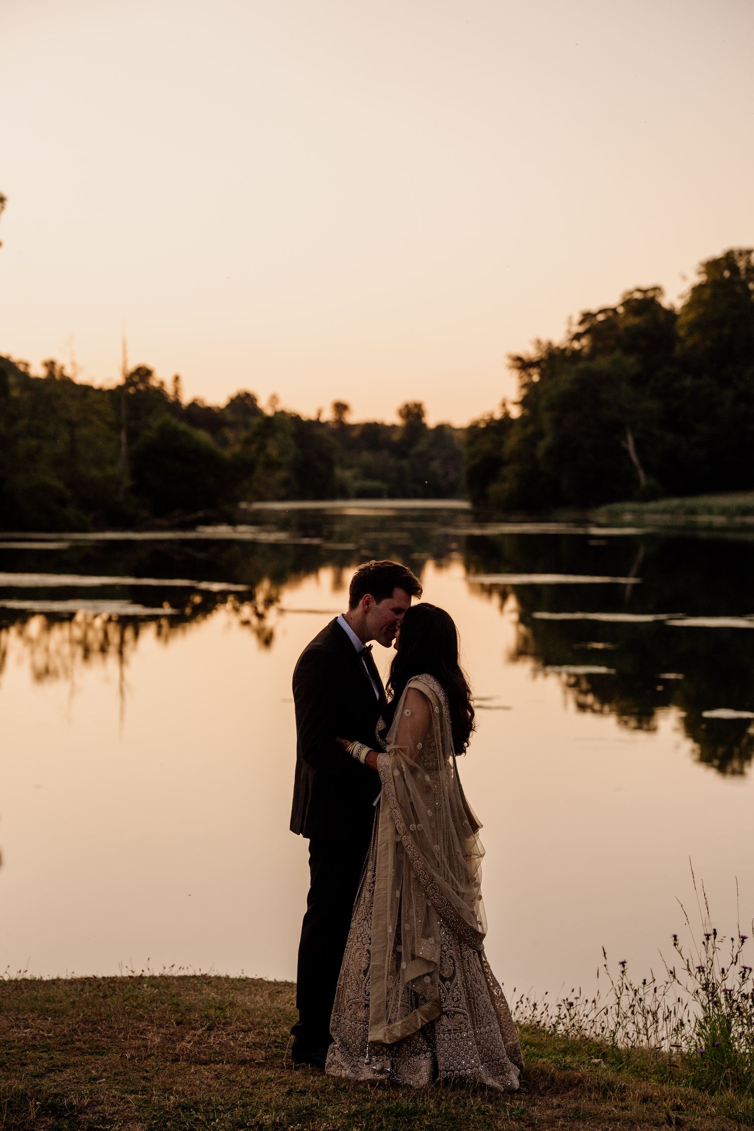 Romantic silhouettes against a serene lakeside sunset with reflections on calm water.