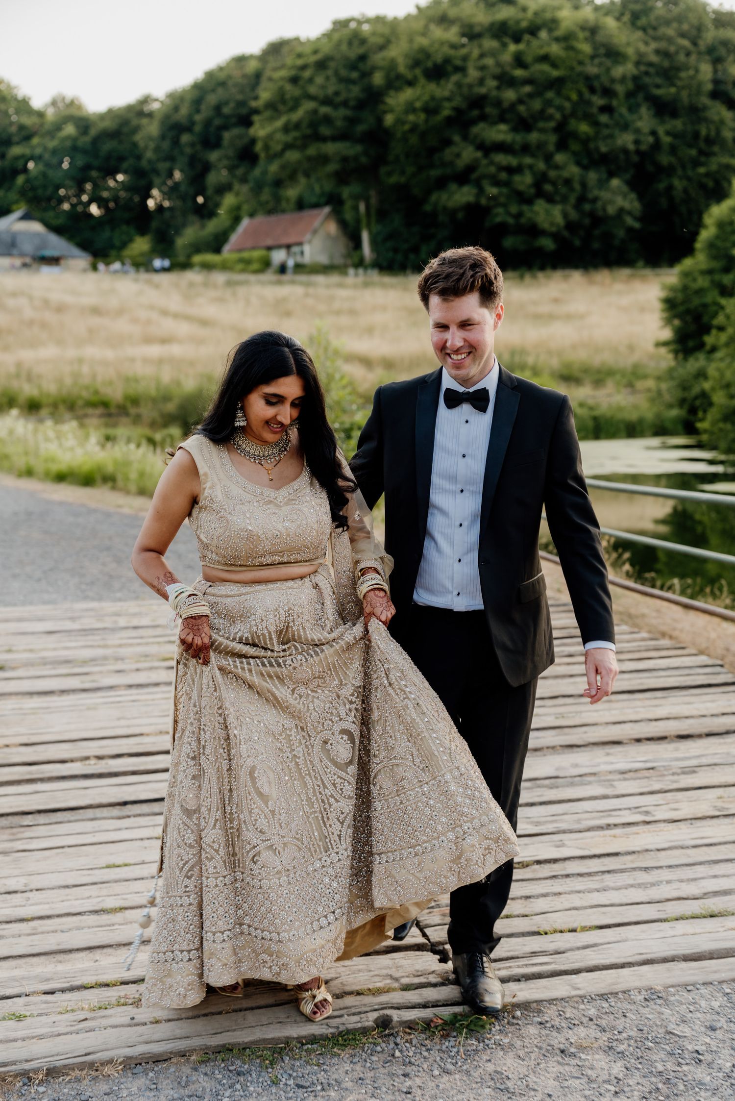 A couple poses on a wooden walkway wearing formal attire including a champagne sequined gown.