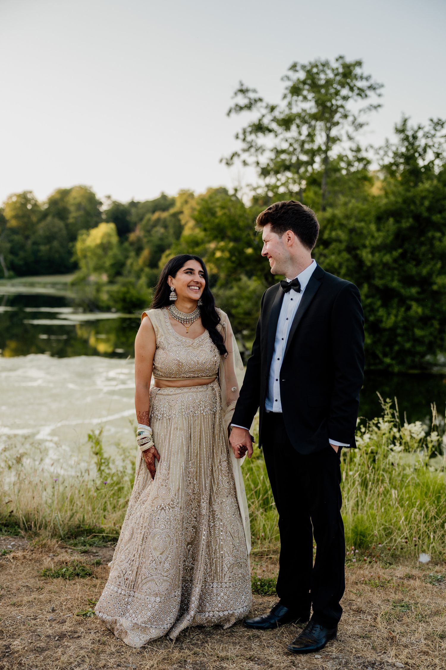 A couple shares a romantic moment by a lake wearing formal wedding attire.