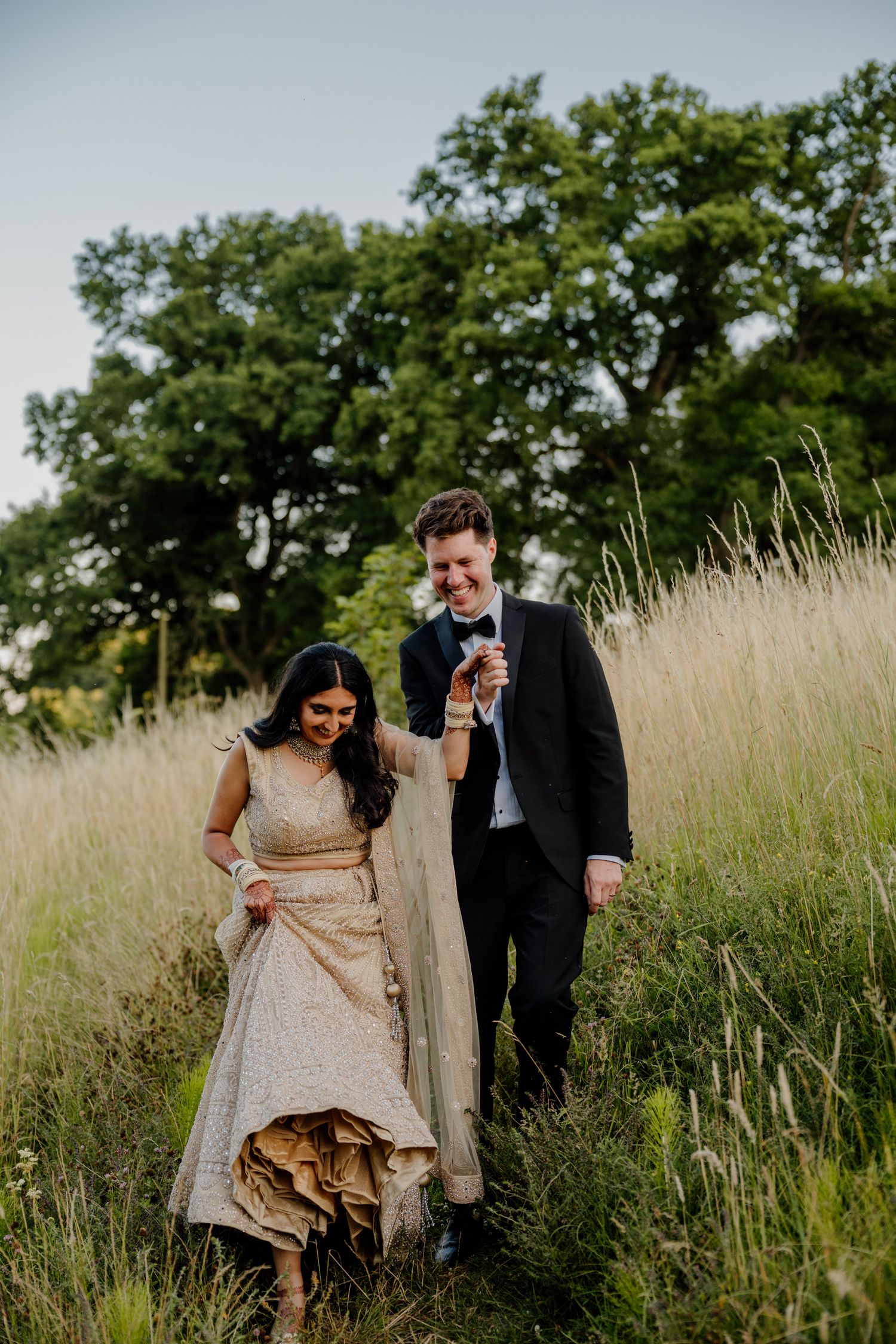 Couple walking together through a sun-lit field of tall grass during an outdoor photo session.