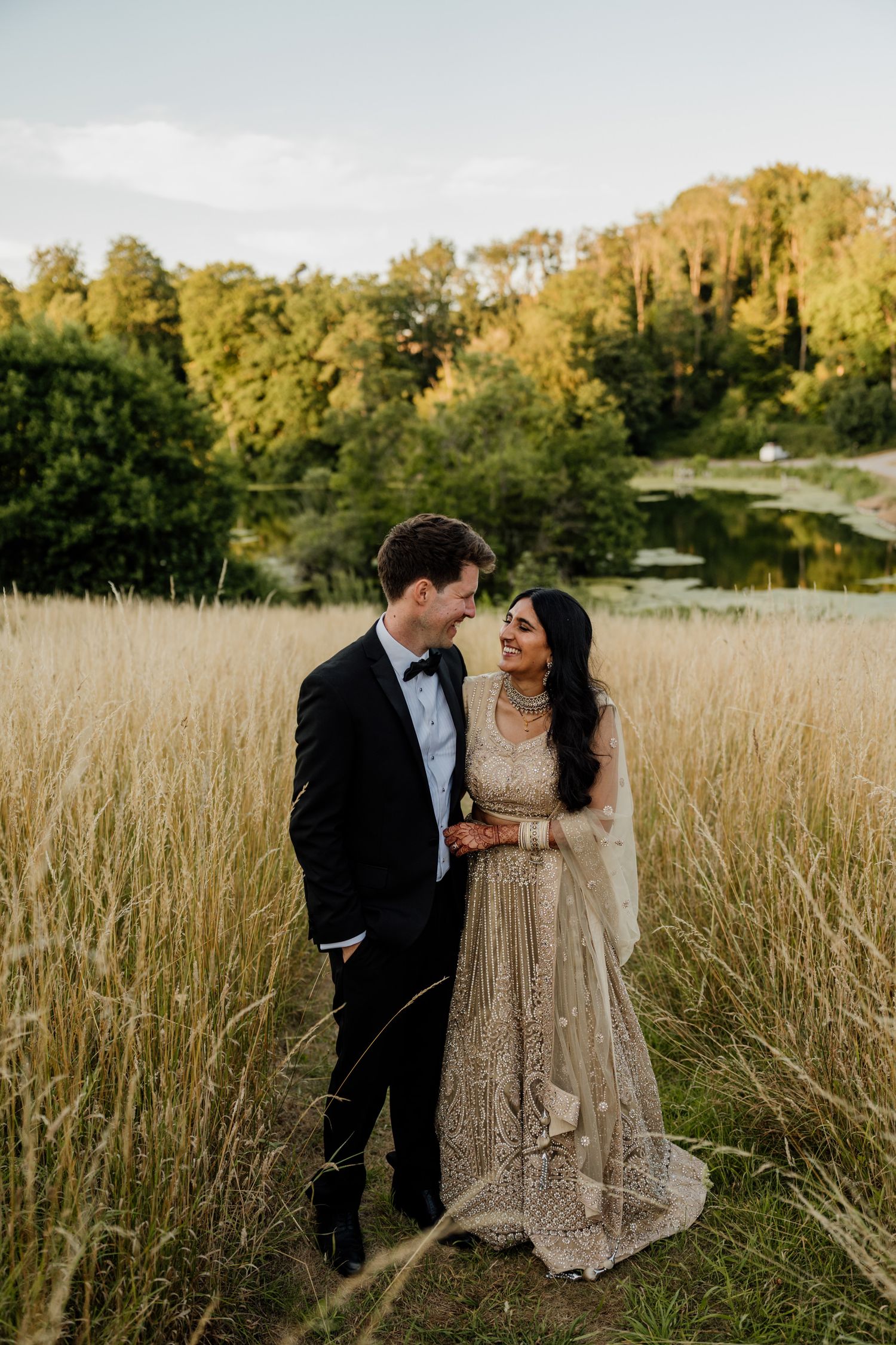 Couple in formal attire sharing a romantic moment in a golden wheat field at sunset.
