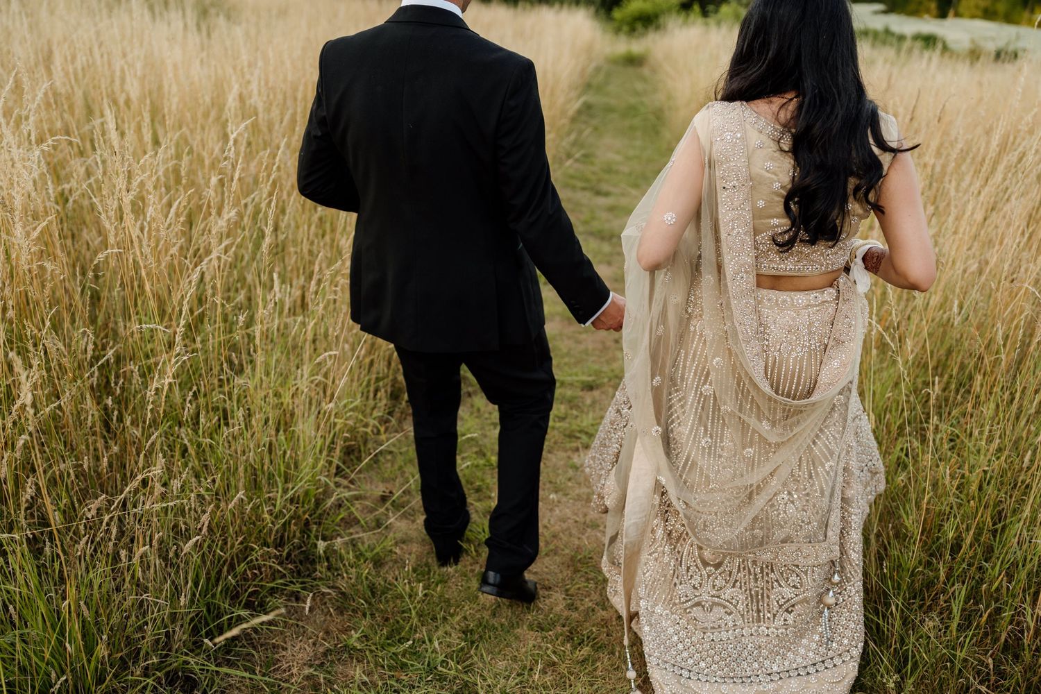 Couple walking through tall grass in formal attire during a golden hour photoshoot.