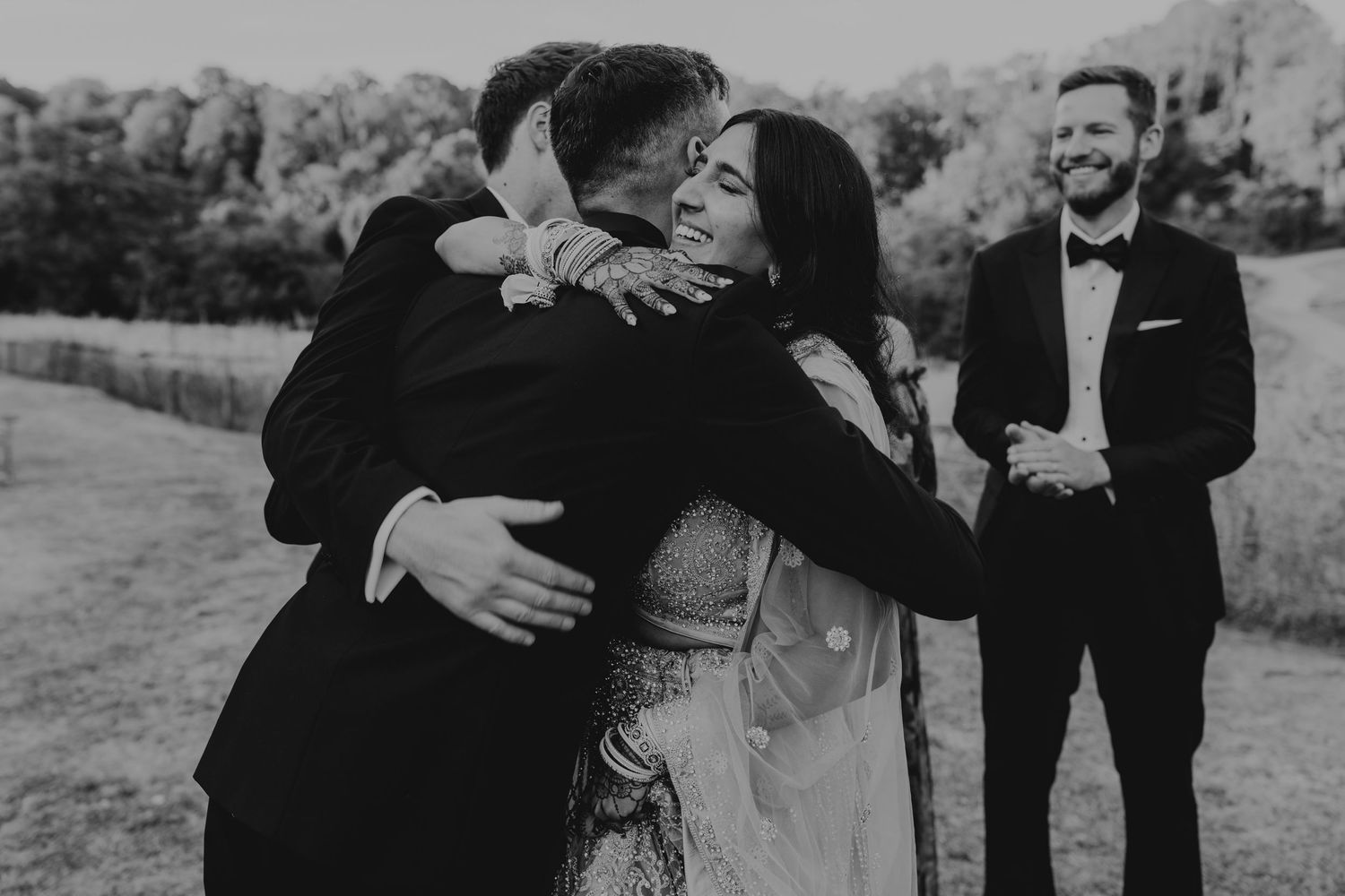 Wedding party members share emotional embraces during an outdoor celebration.