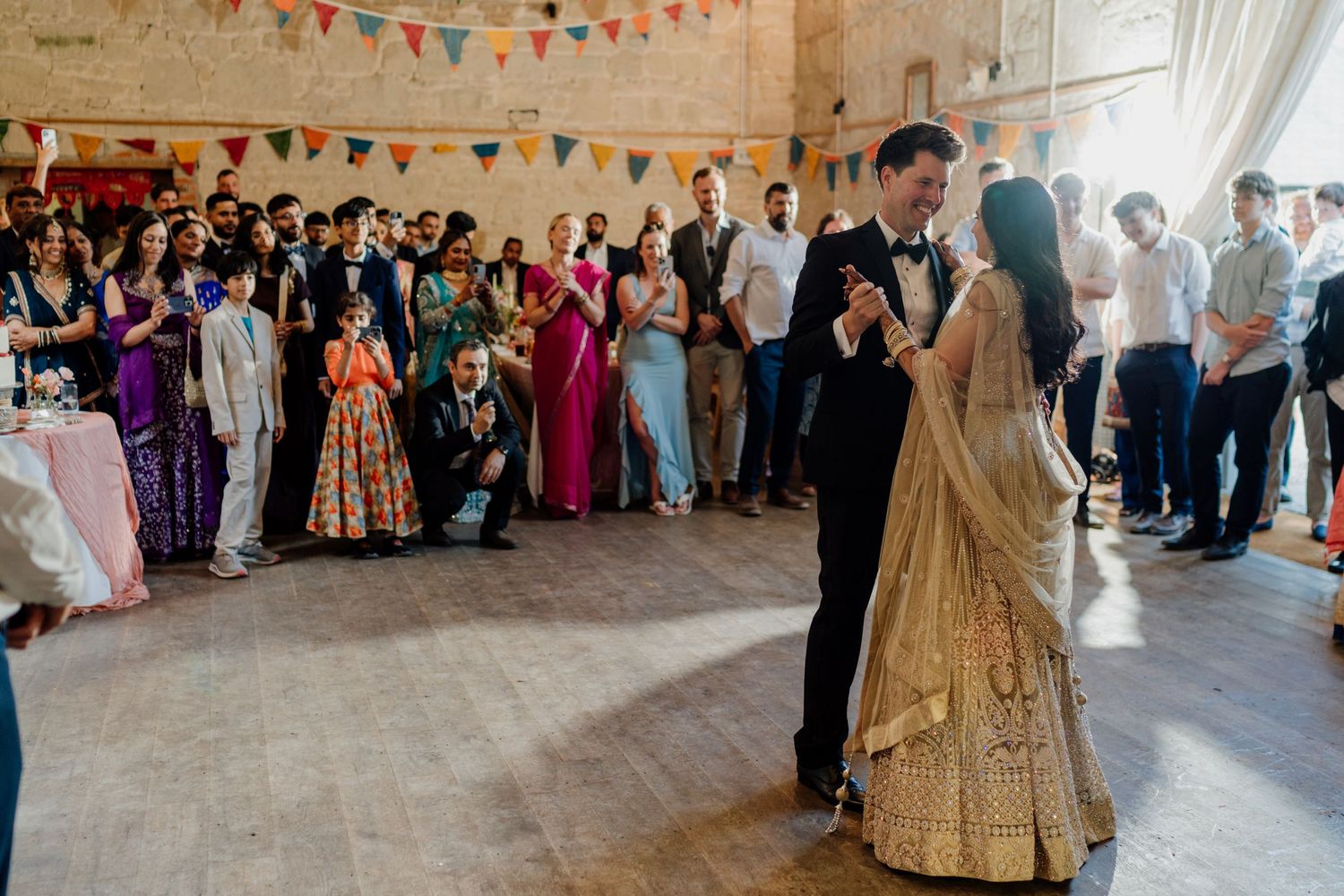 Wedding celebration in a historic stone hall with guests dancing under festive bunting decorations.