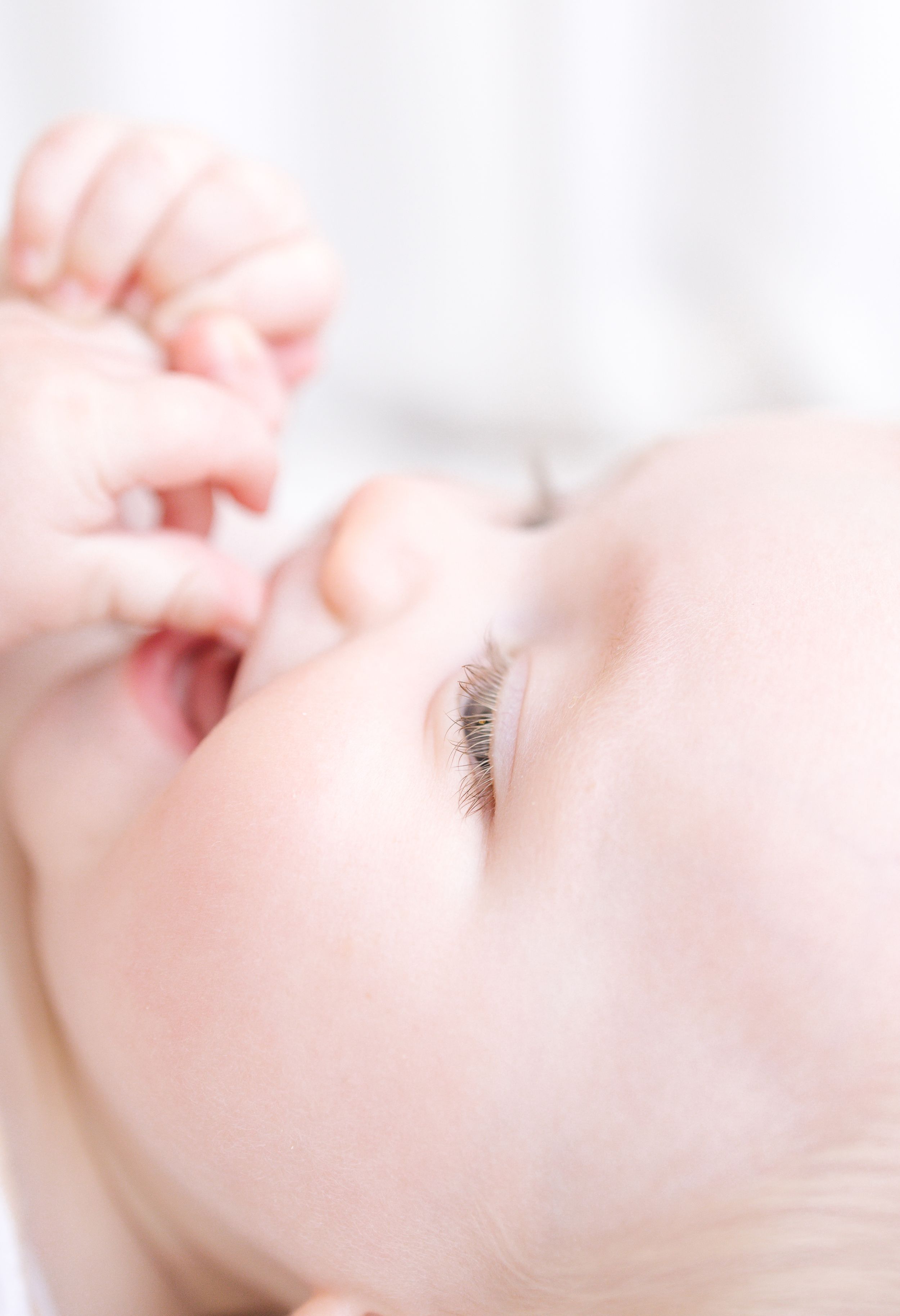 Close-up of a peaceful baby with delicate eyelashes, soft skin, and tiny fingers near their mouth.