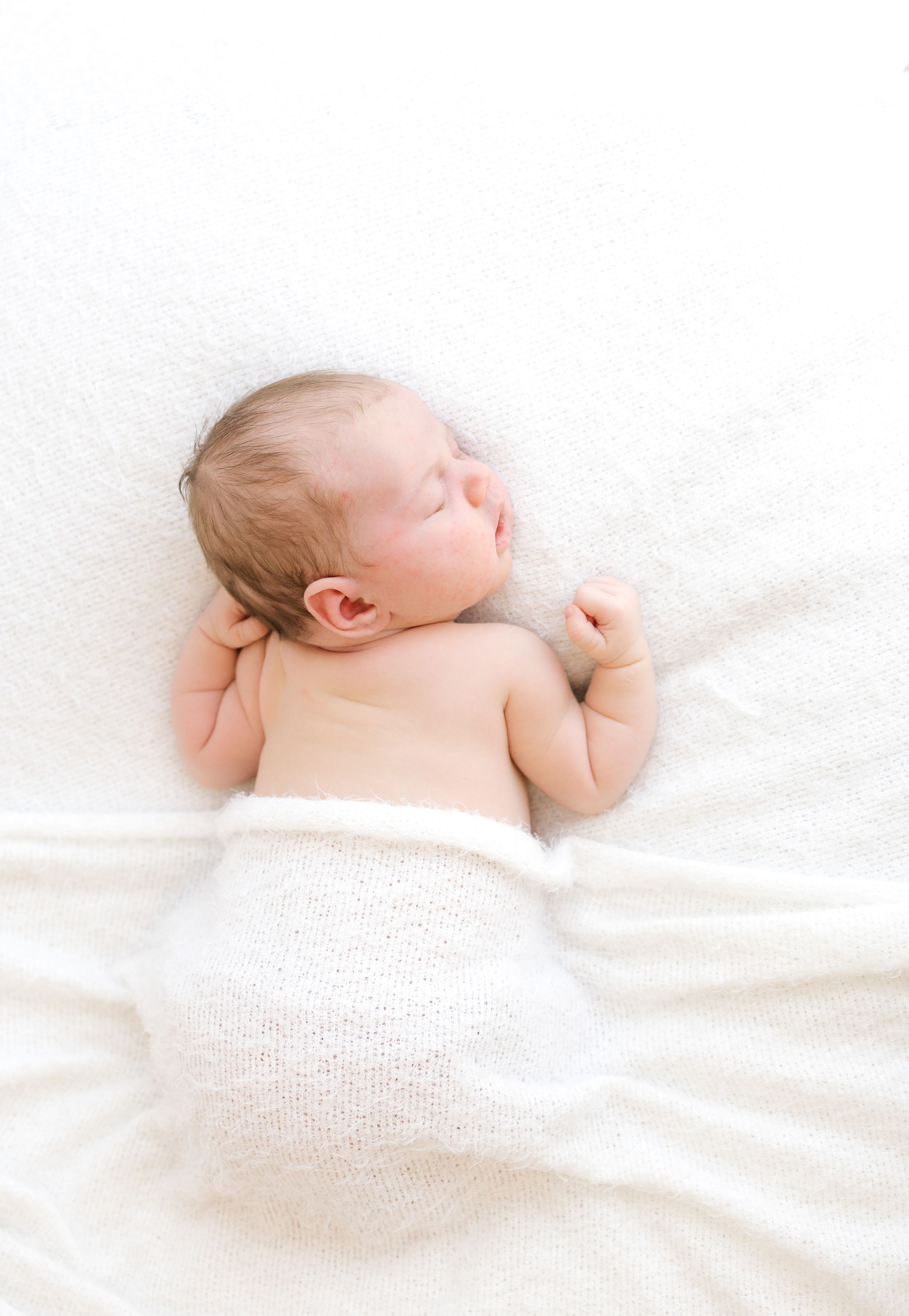 Peaceful newborn baby sleeping on white blanket, wrapped in soft white knit wrap, perfect newborn photography.