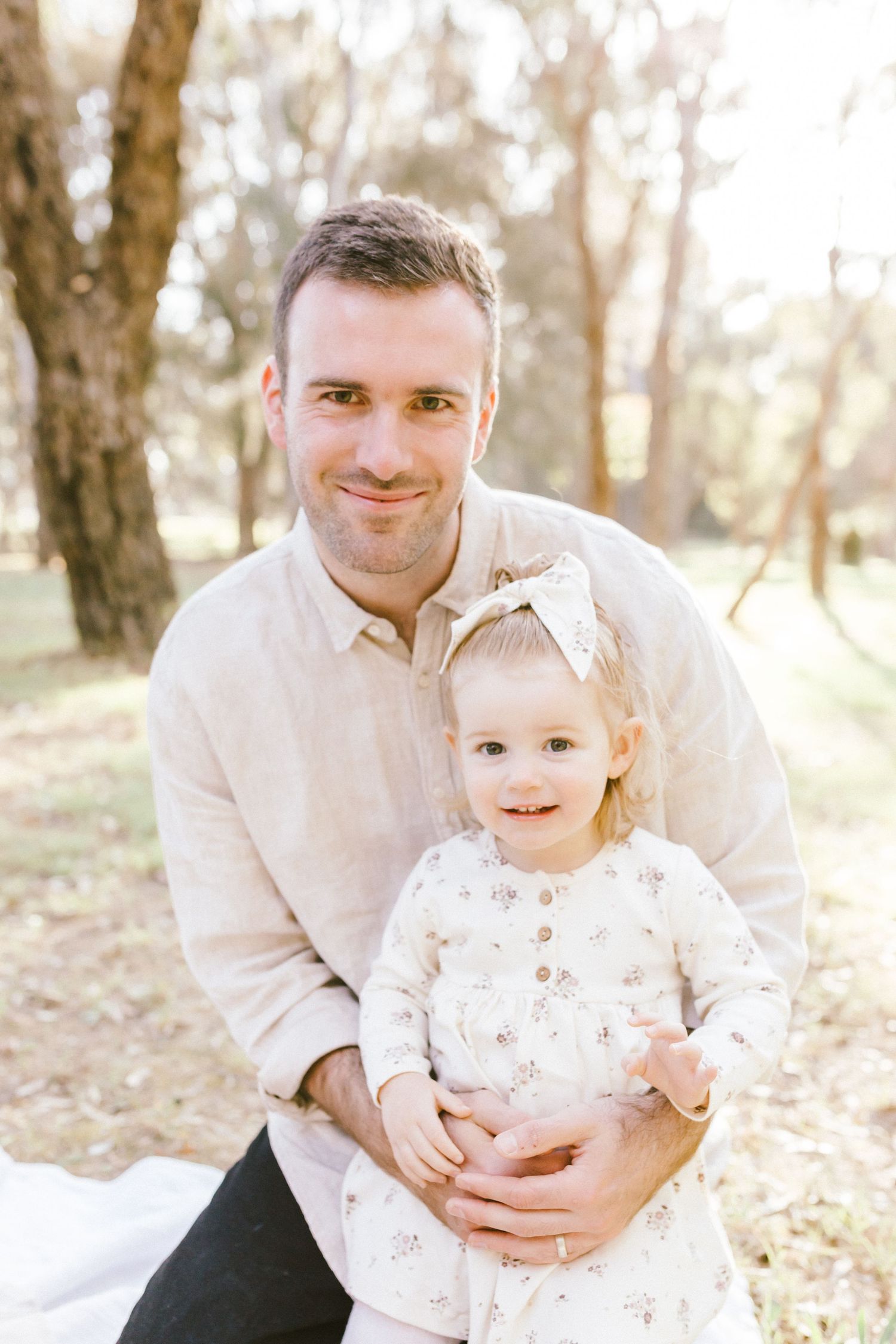 Tender outdoor family portrait moments in matching light colored outfits among trees.