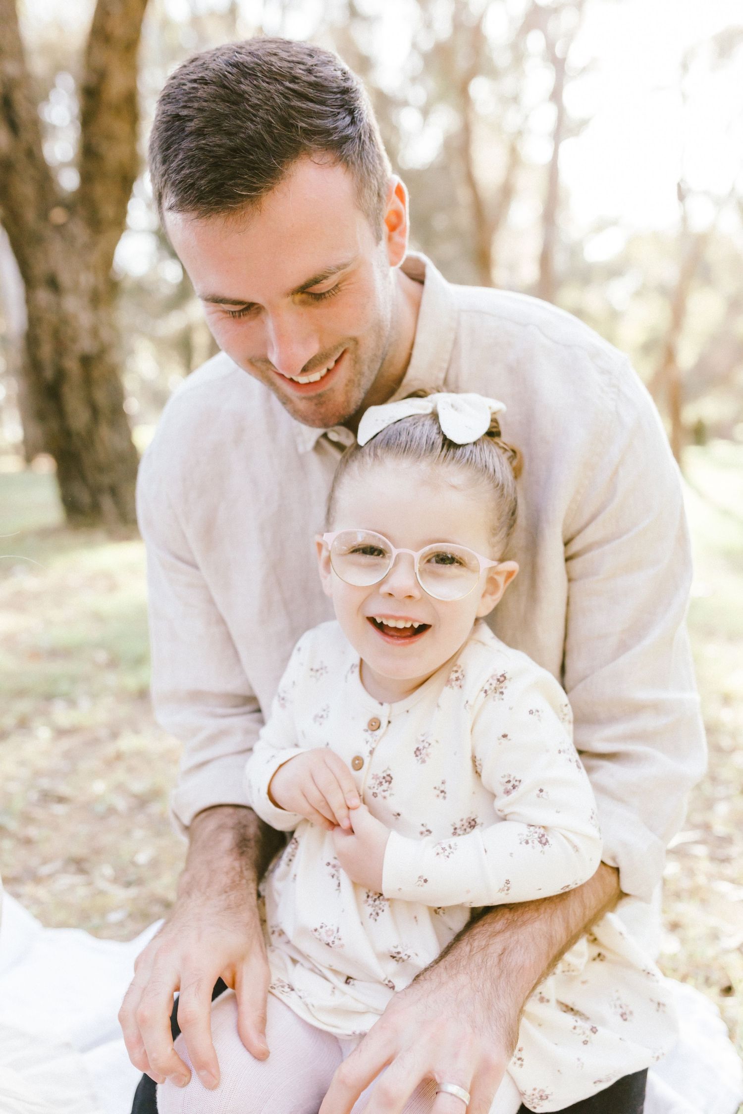 A father and child share joyful laughter during a tender outdoor family photo session in natural sunlight.