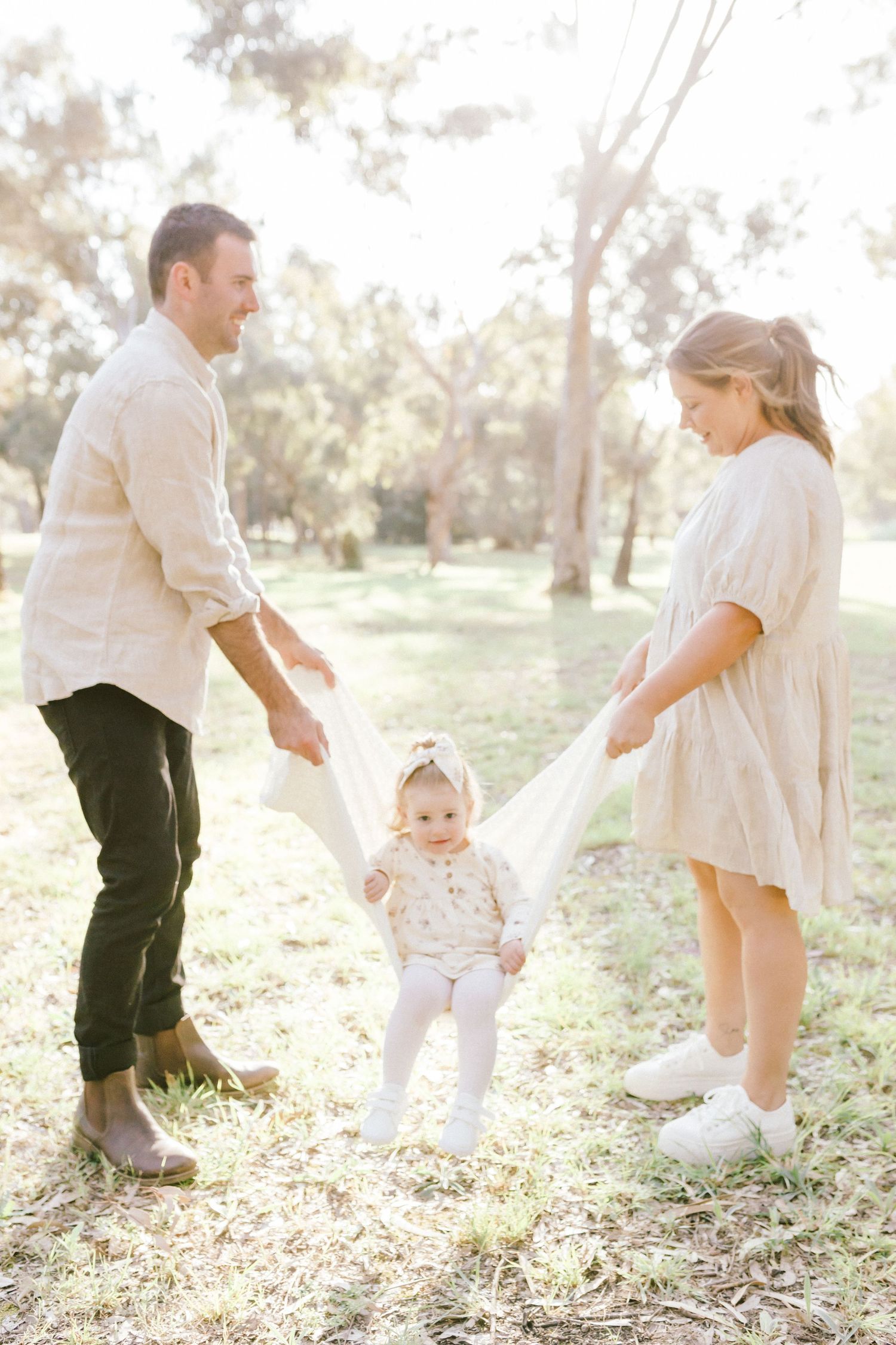 Family playing and dancing together in a sunlit outdoor setting with trees in the background creating joyful moments.