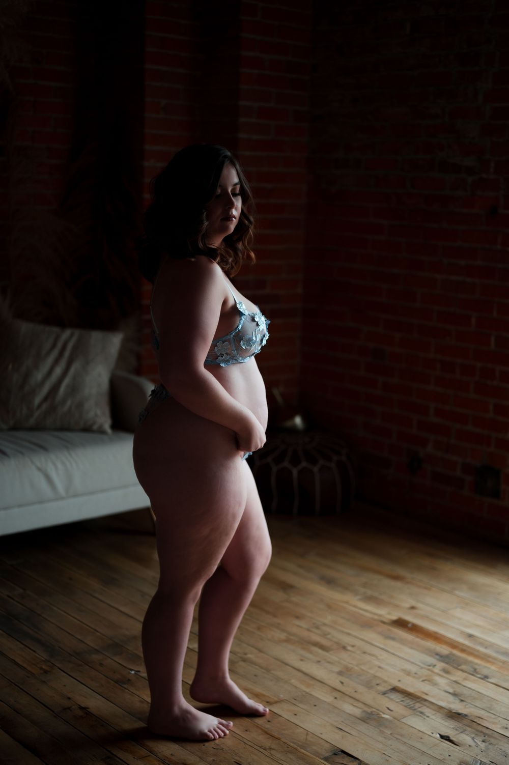 A silhouetted figure stands near a brick wall in intimate maternity photos showing bare skin and dark shadows.