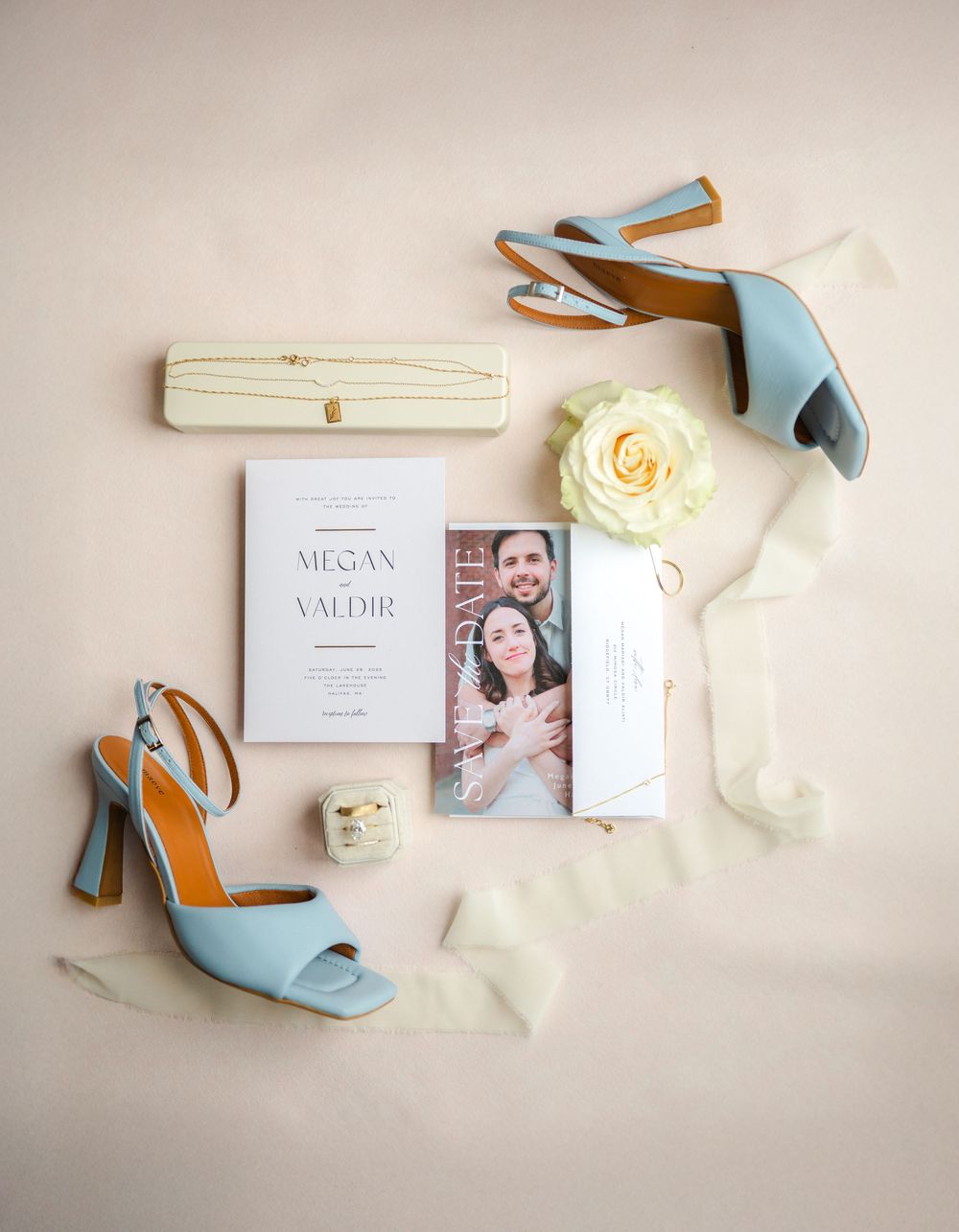 A wedding detail flat lay including invitation items including light blue shoes, ivory ribbons, and white stationery laid out aesthetically.